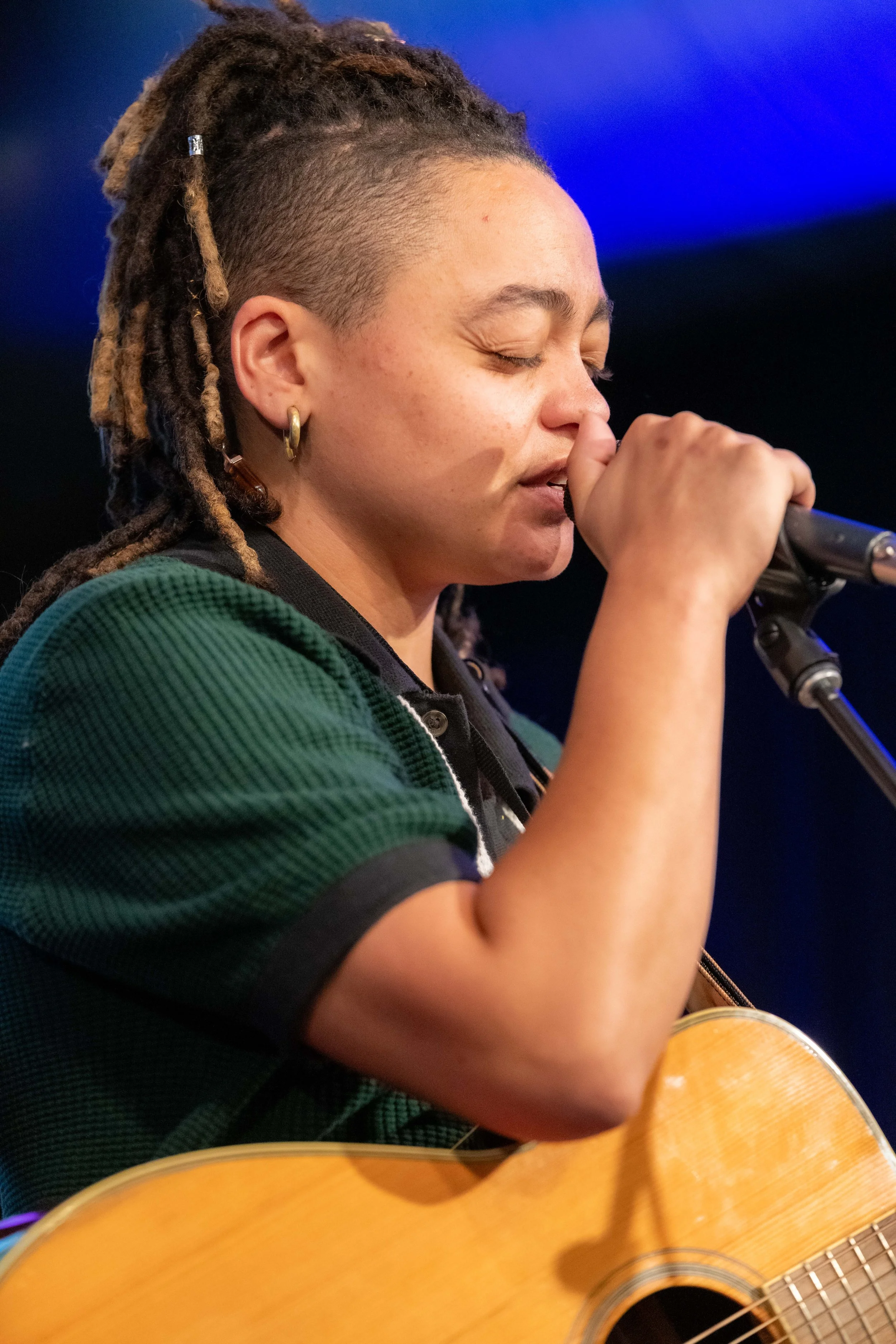 A human with a guitar holds onto a microphone and sings into it.