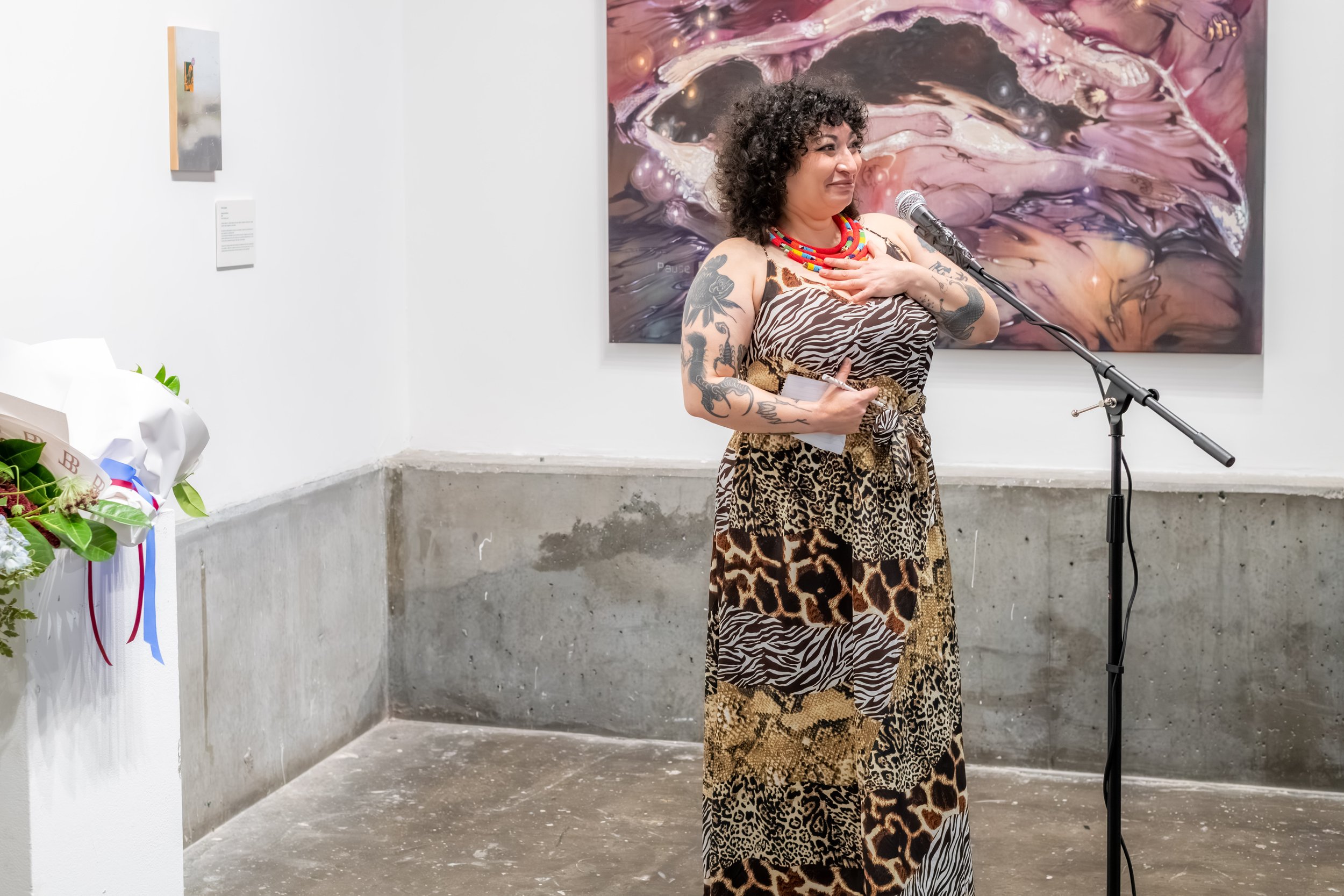 A human holds their hand to their chest as they speak into a microphone.