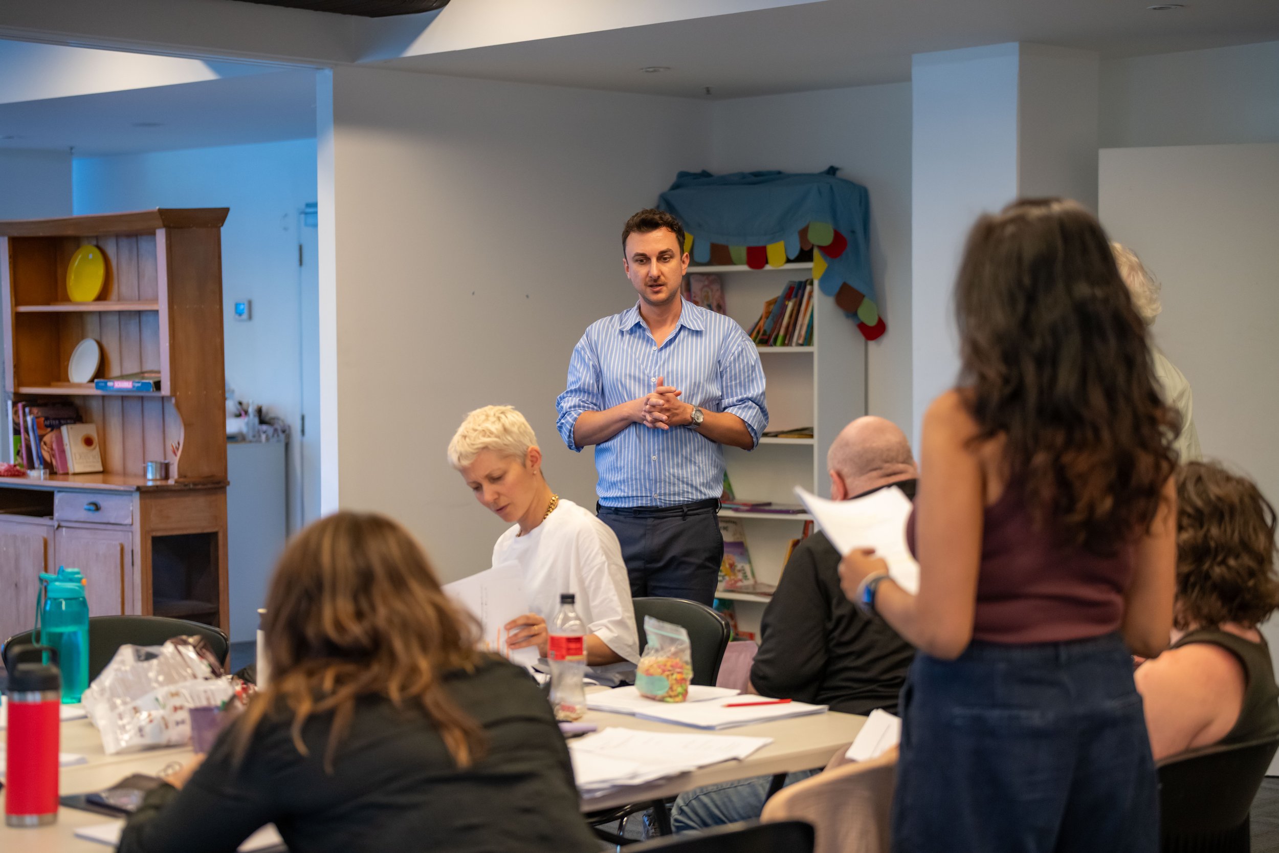 Several human work around a table. Two humans are standing on opposite sides whilst the others sit.