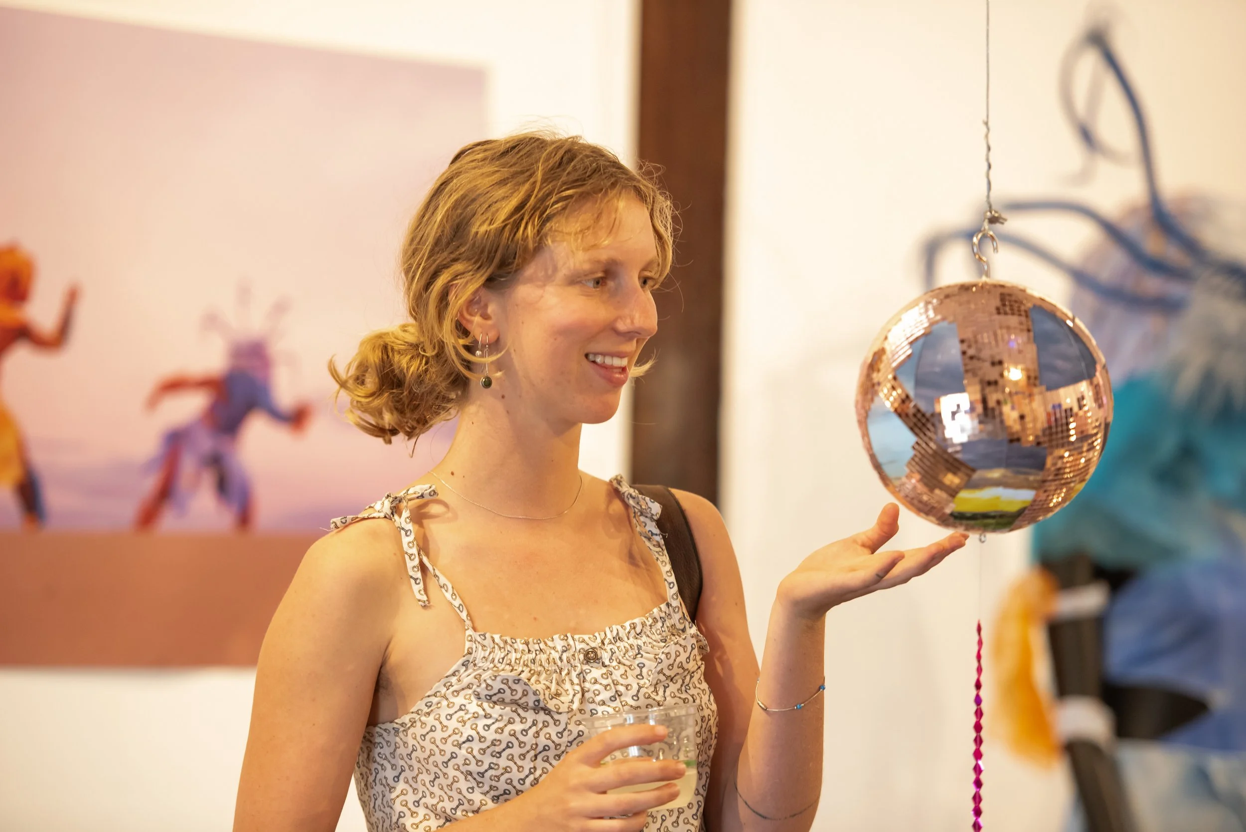 A human smiles and touches a deconstructed mirror ball suspended in the air.