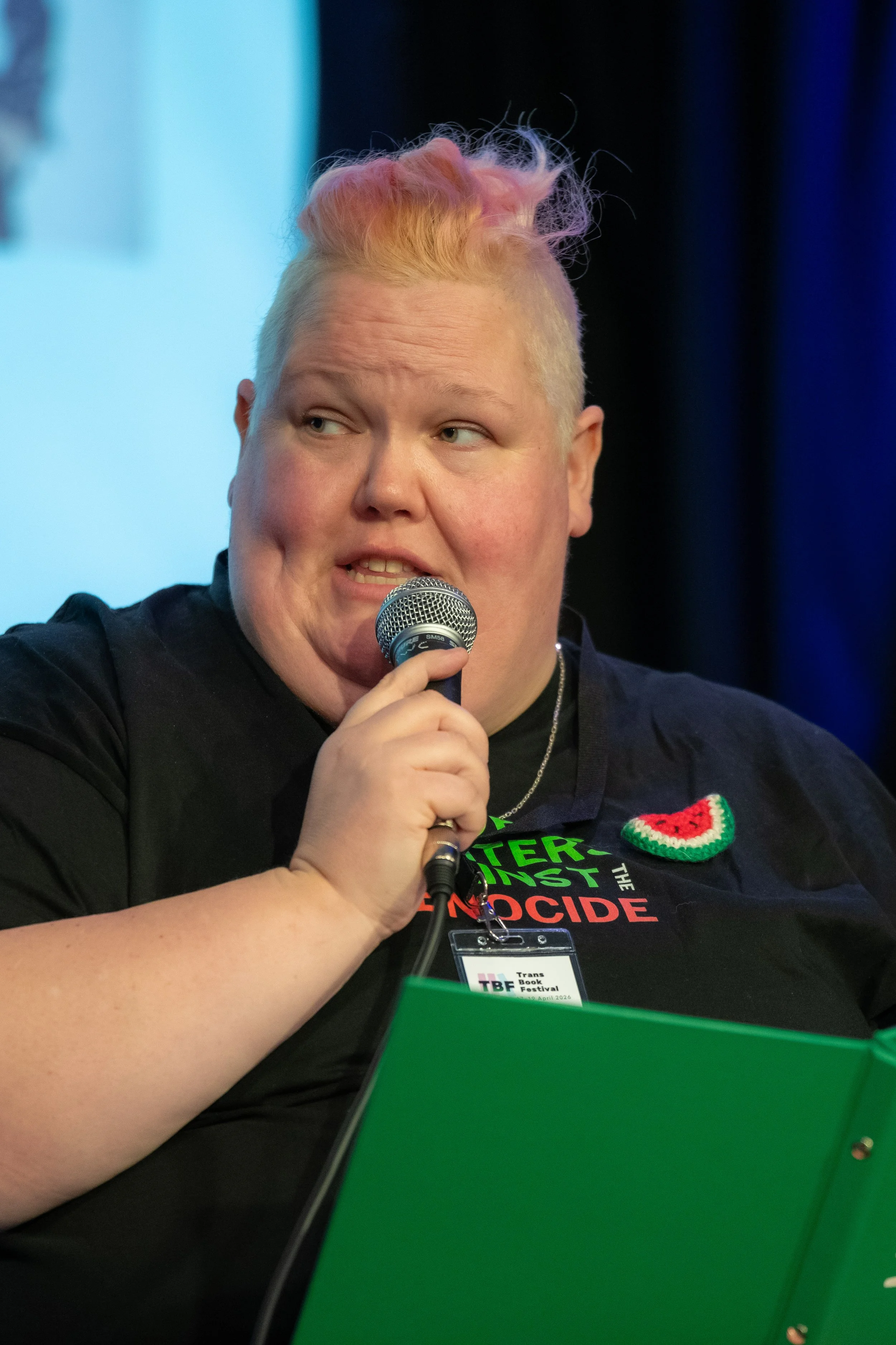 A panelist with pink hair speaks into a microphone.