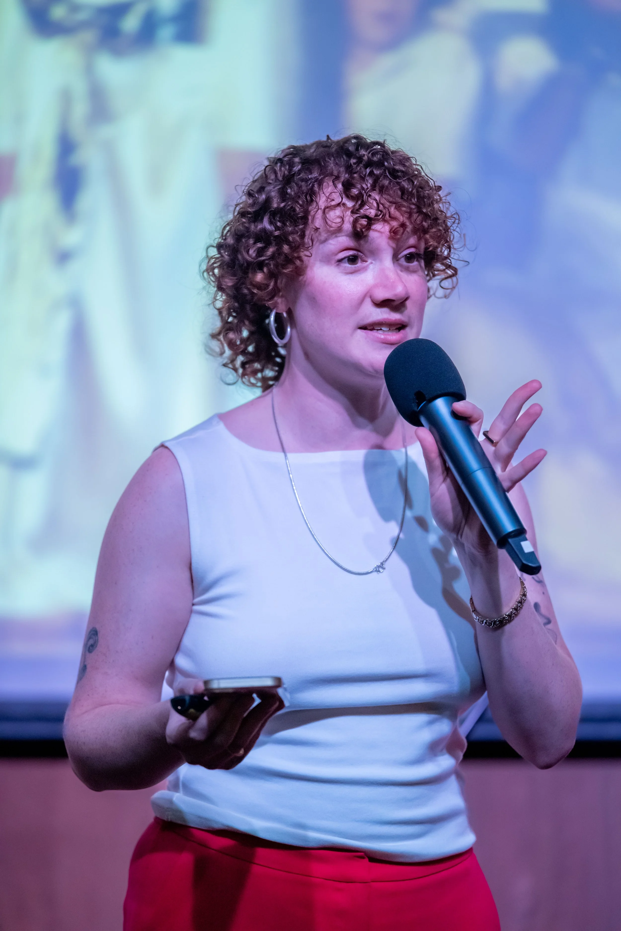 A human with curly hair speaks into a microphone.