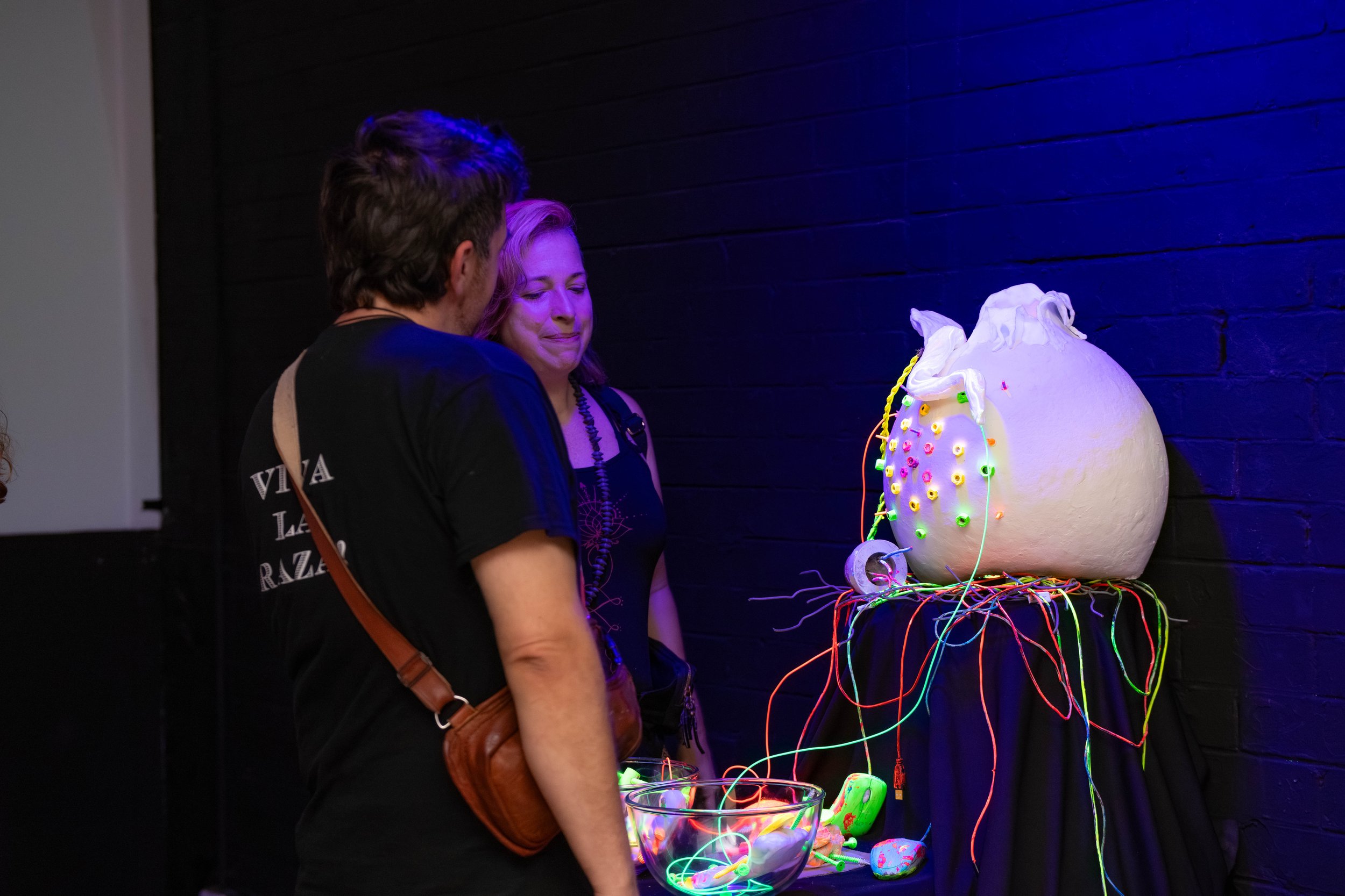 The artist and another human stand near their sculptural piece and talk.