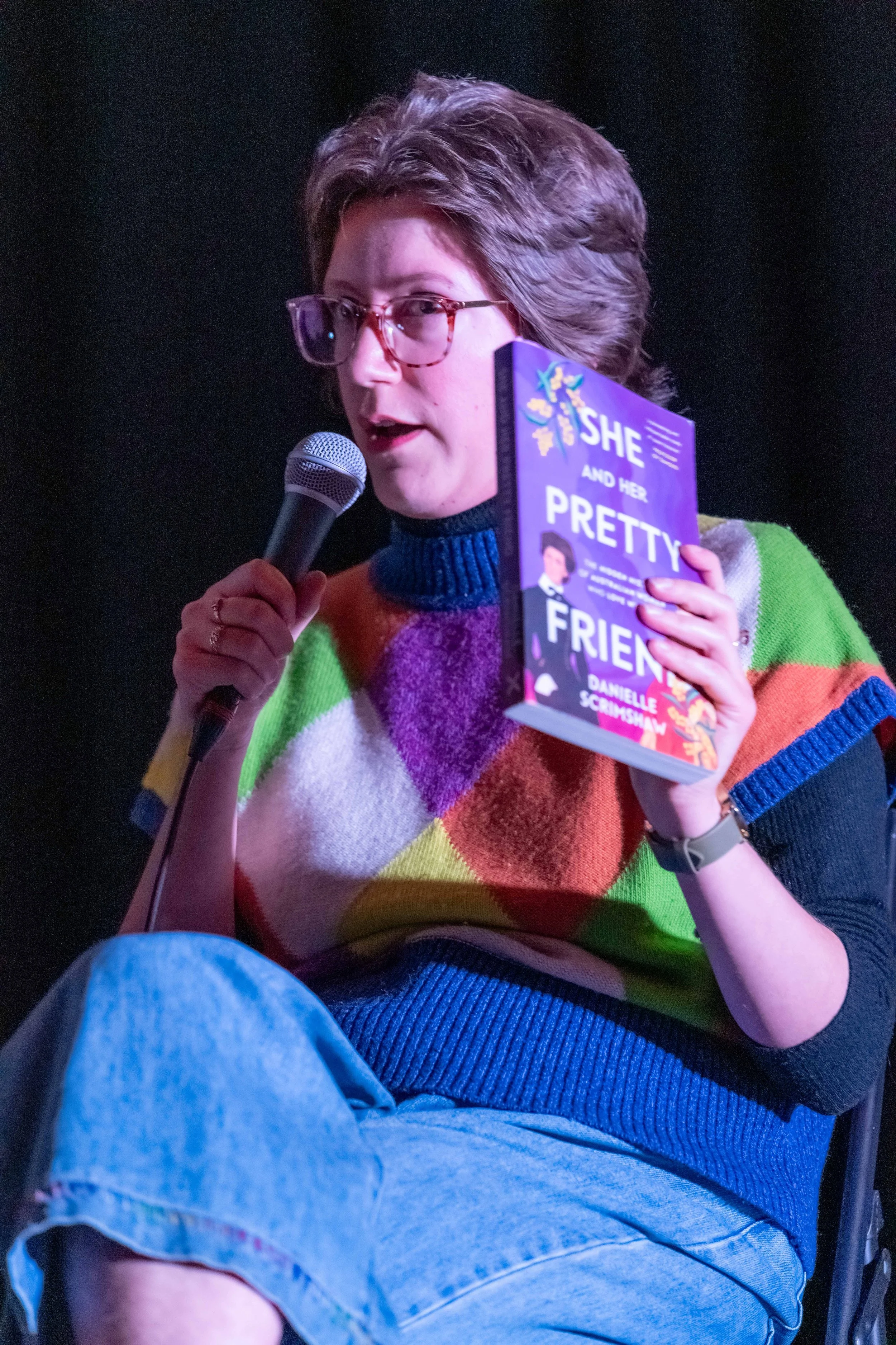 Danielle Scrimshaw holds up a book and speaks into a microphone.