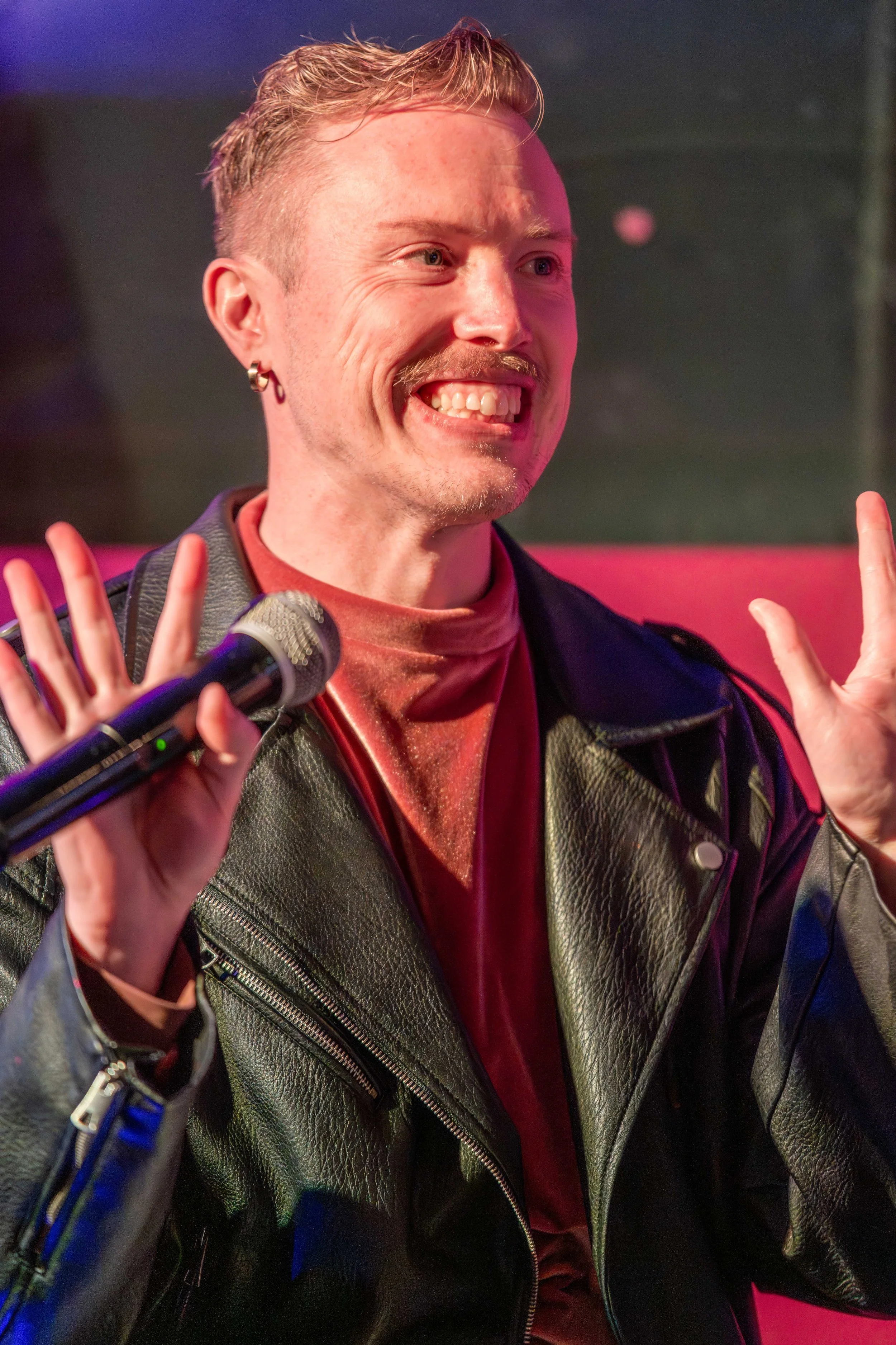A human holds a microphone and waves at the unseen audience.