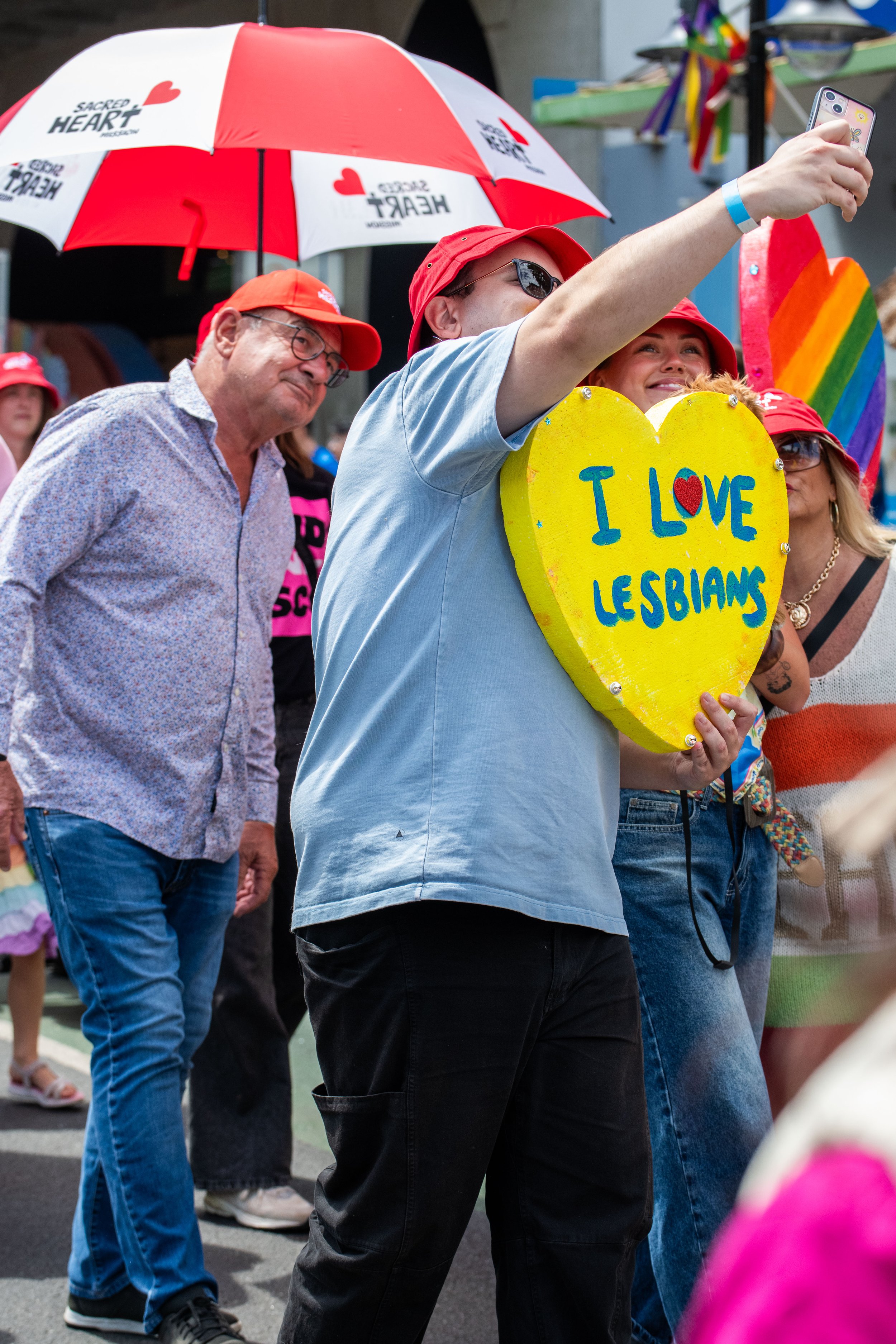 Humans pose for their phone selfie and hold up a love heart "I love lesbians".