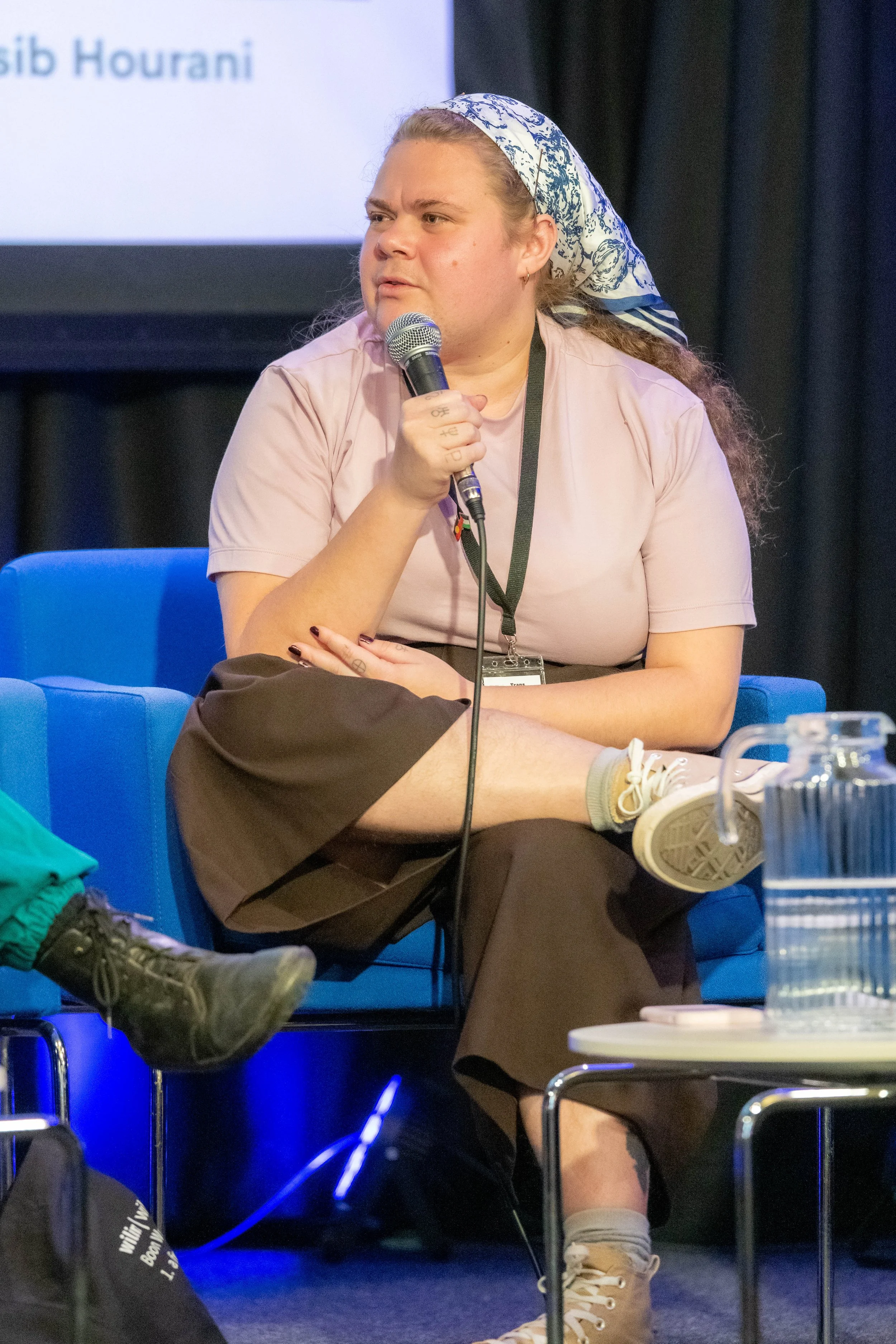 A panelist wearing a head scarf speaks into a microphone.