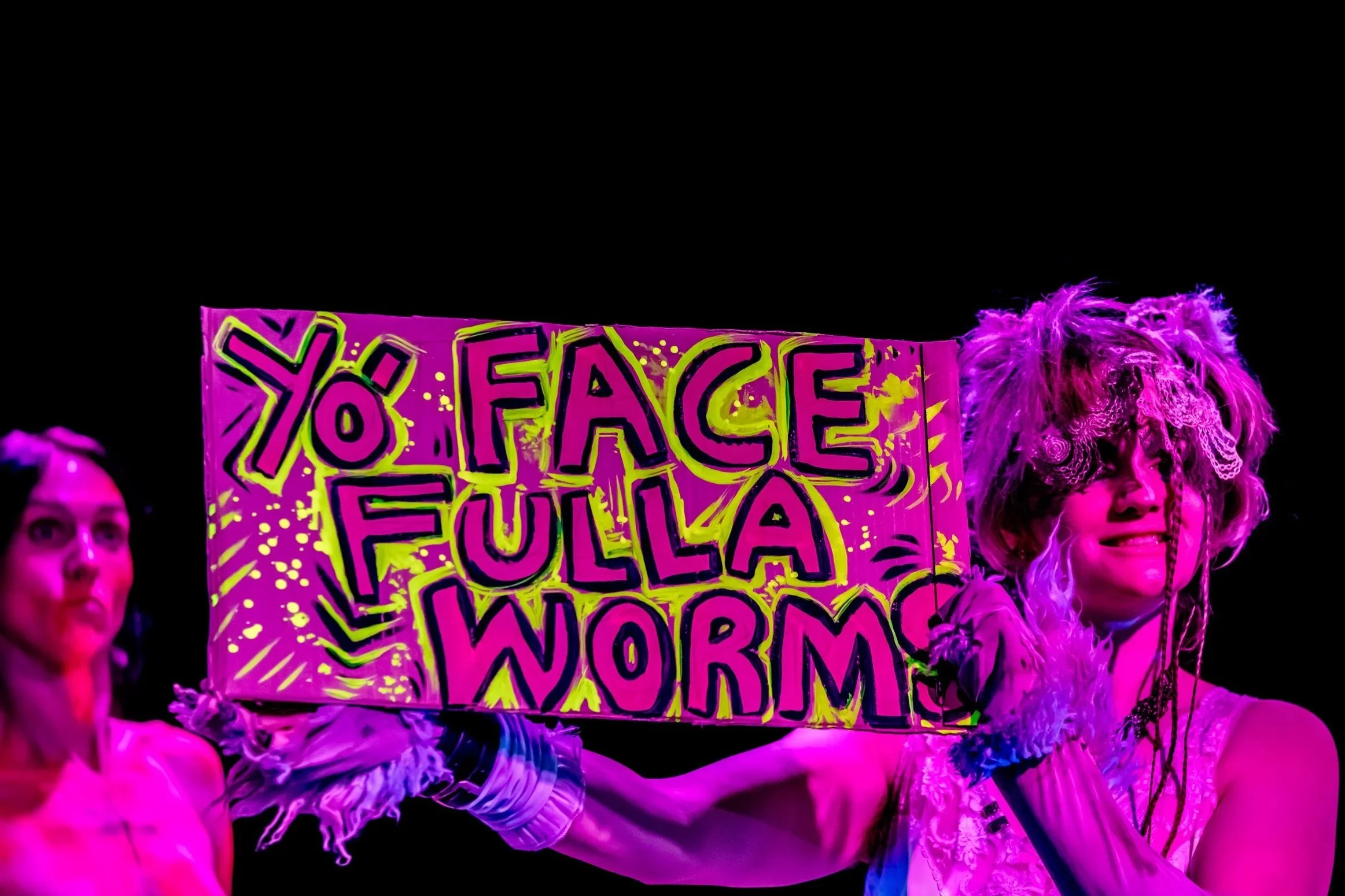 A performer holds up a sign that reads "Yo' Face Fulla Worms".
