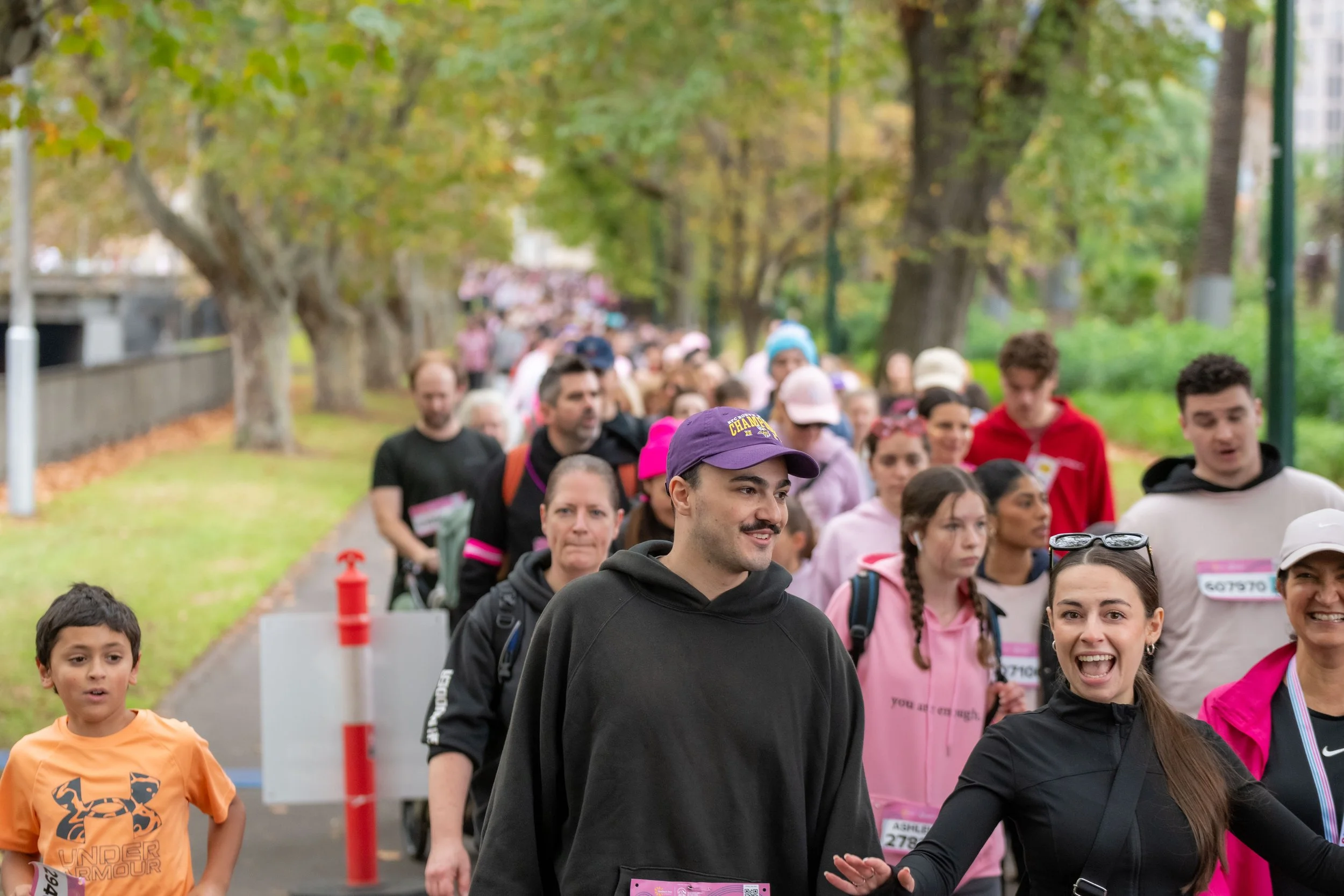 A tree lined street filled with racegoers wearing pink.