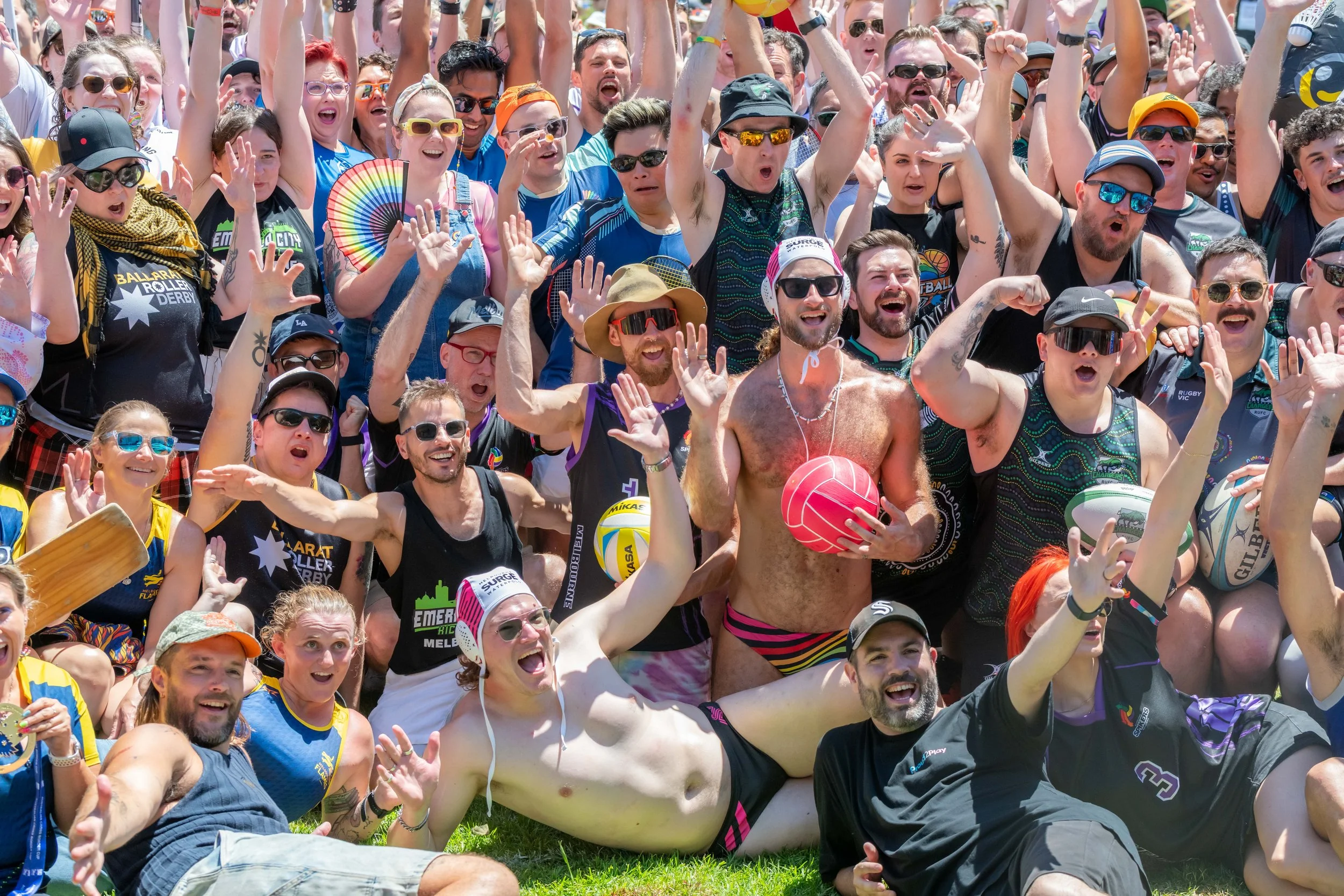 A large group of sports players lay on the grass, sit, and stand and raise their arms in the air.