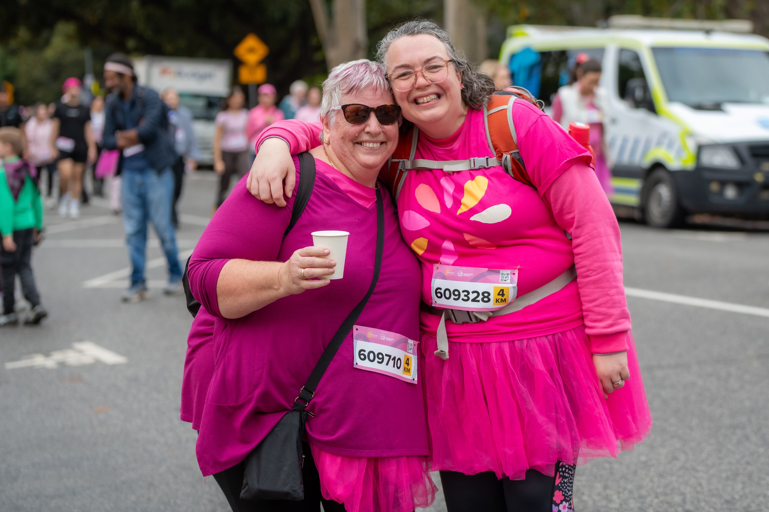 Two racegoers wearing pink smile at the camera.