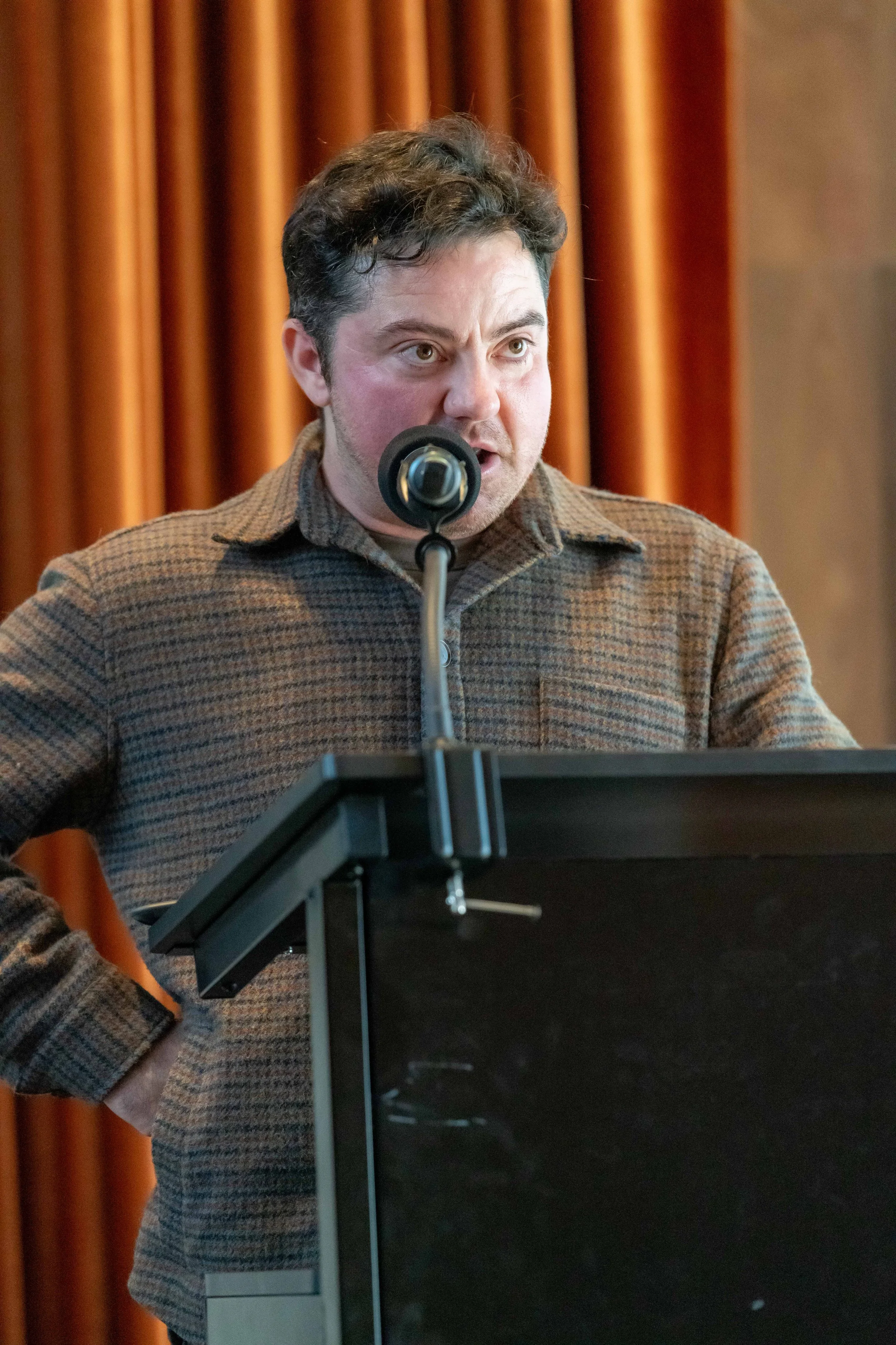 Sam Elkin holds a hand on hip and speaks into a microphone.