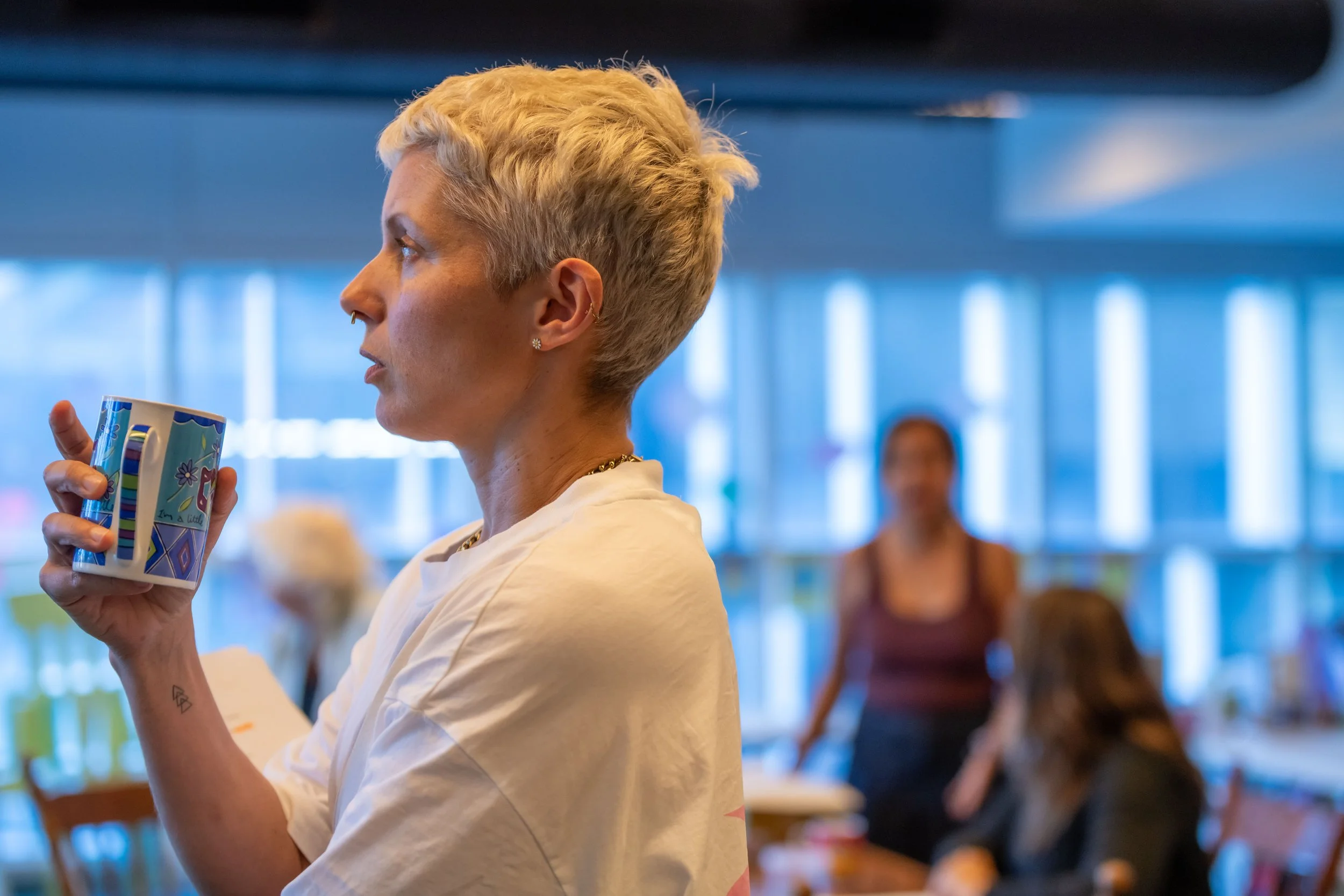 A human holds a mug and looks off in the distance whilst standing side on to the camera.