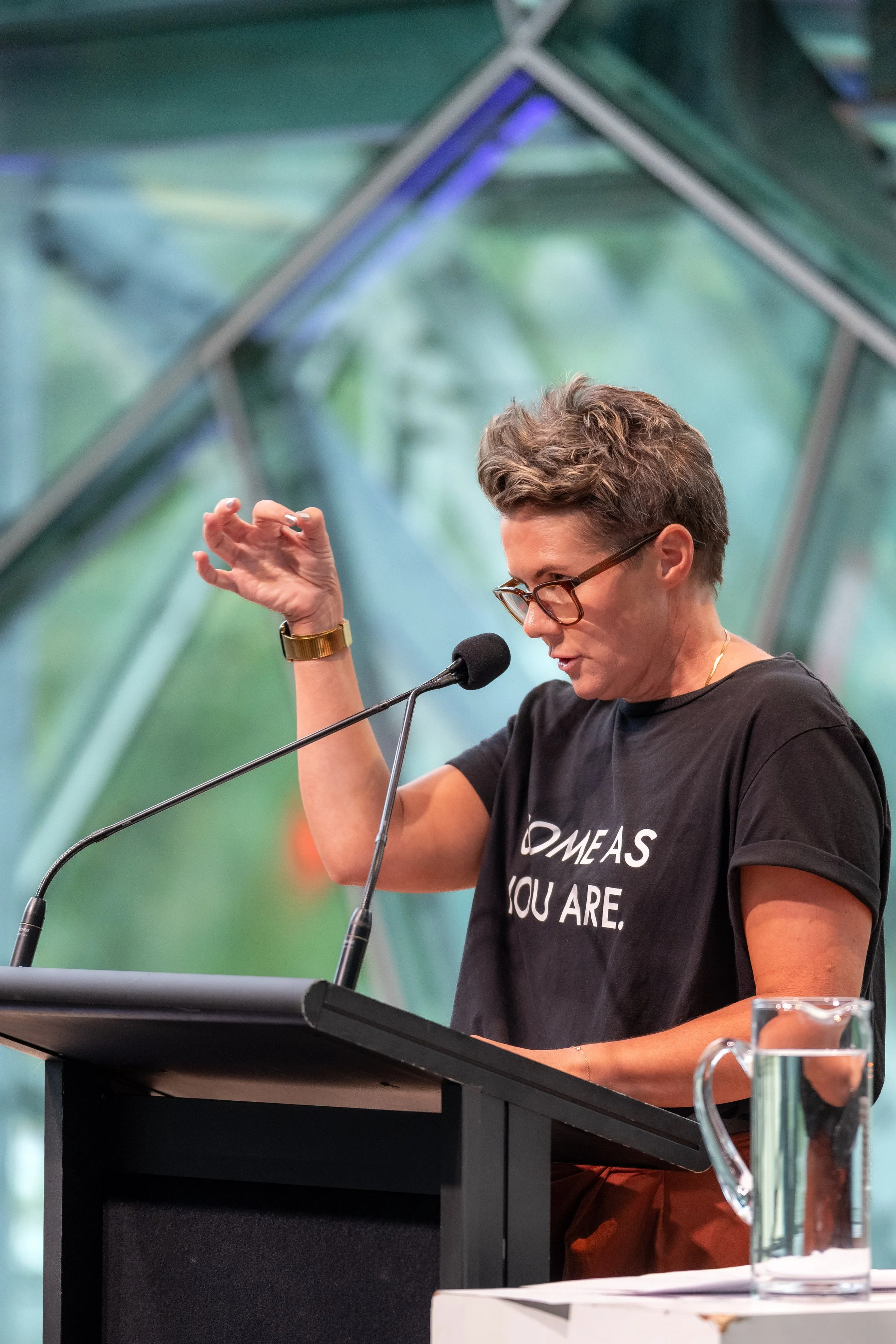 Bec Goddard looks over their glasses and gesticulates with a hand.