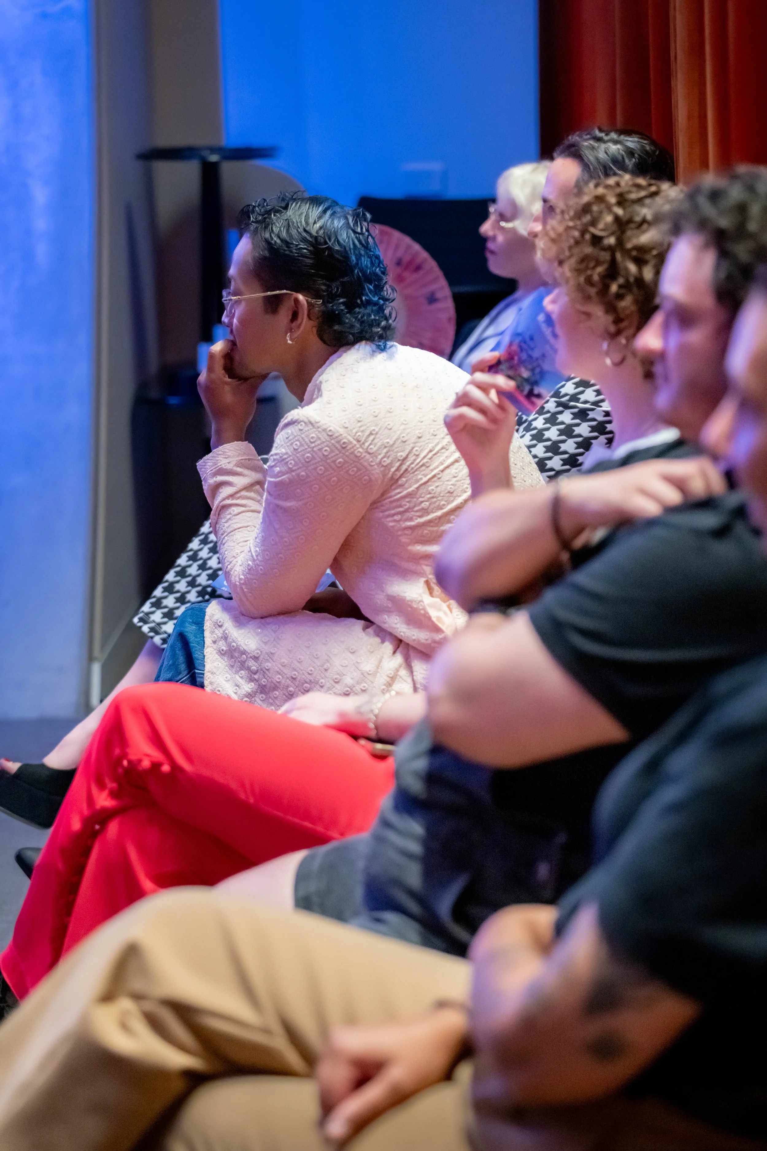 A human wearing white leans forward intently as they listen to a speaker offscreen.