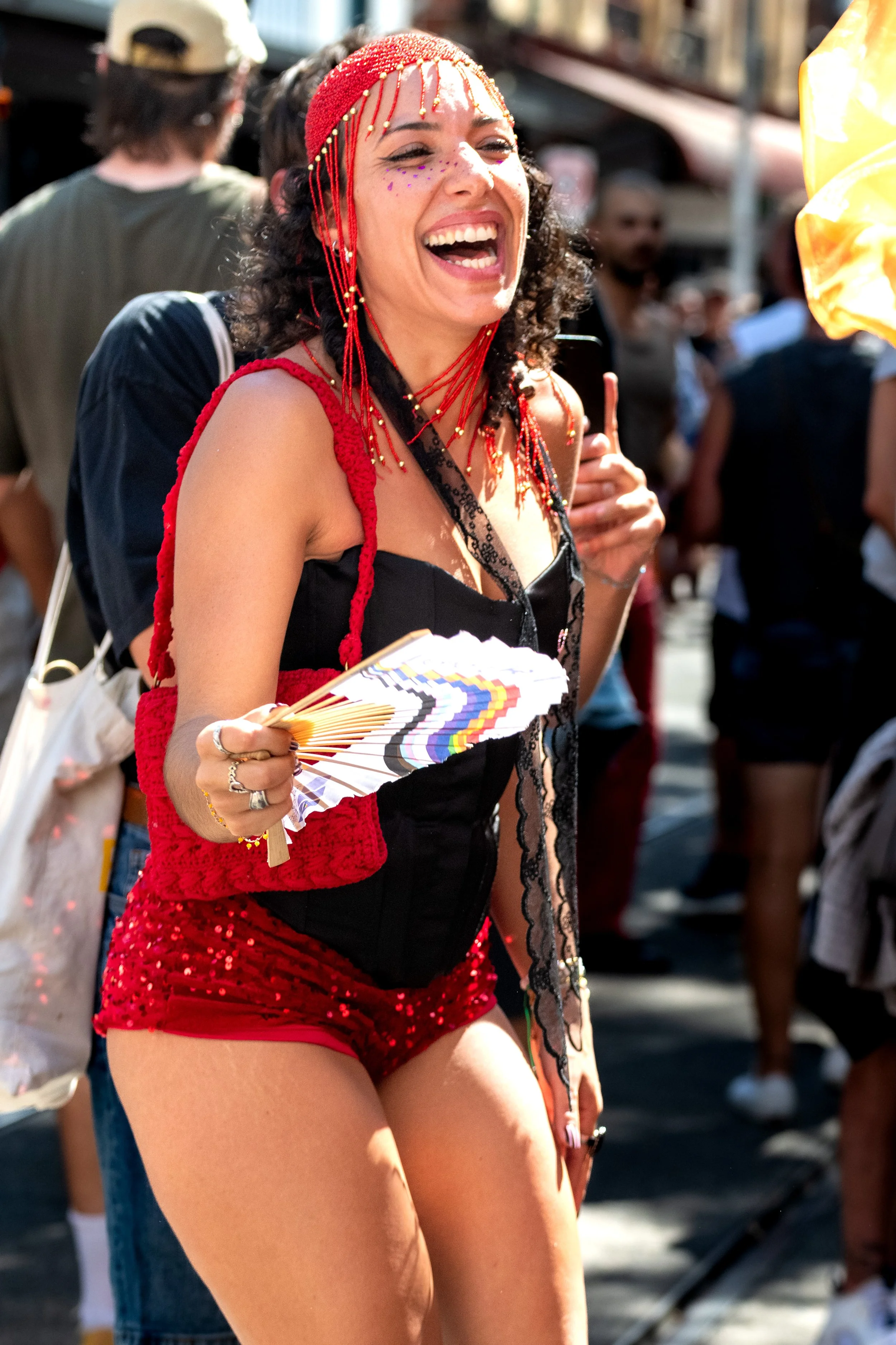 A human wearing red glitter pants holds a fan and laughs.
