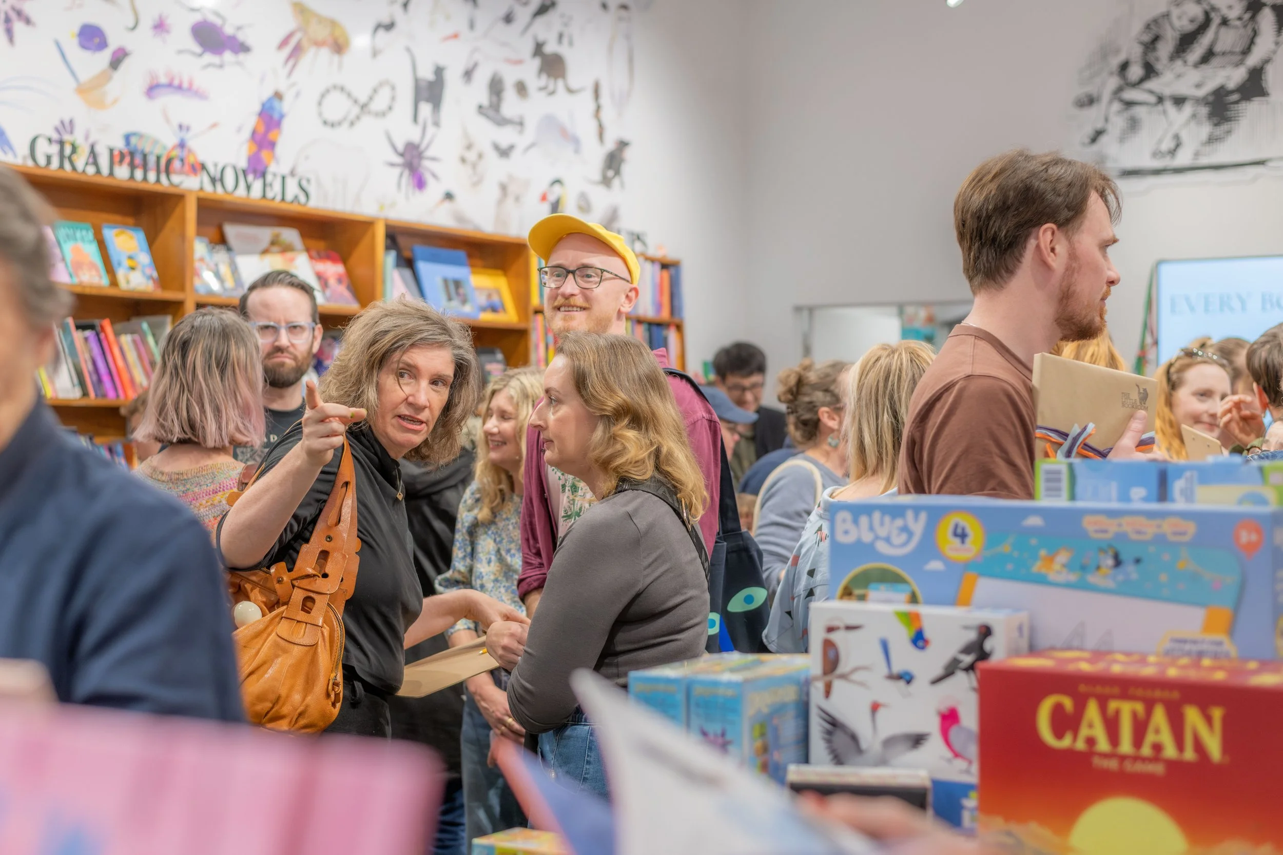 Large masses of humans chat throughout the bookstore. One is pointing.