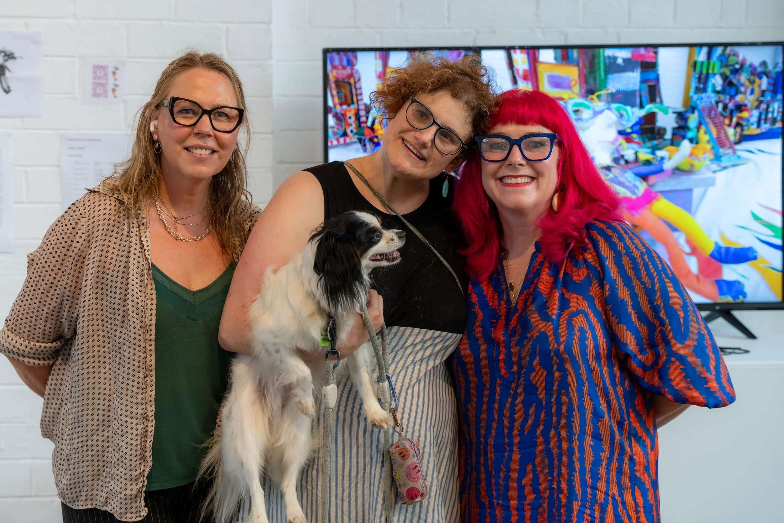 Three humans pose for the camera. The middle human is holding a small dog.