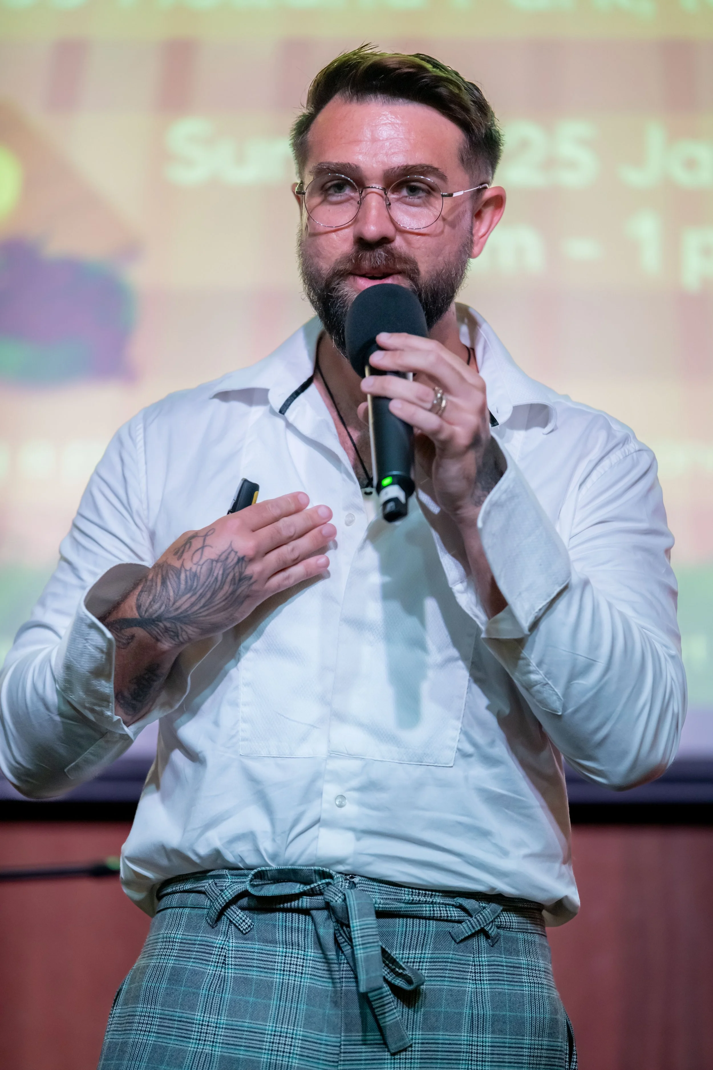 A human wearing glasses and a white shirt speaks into a microphone.