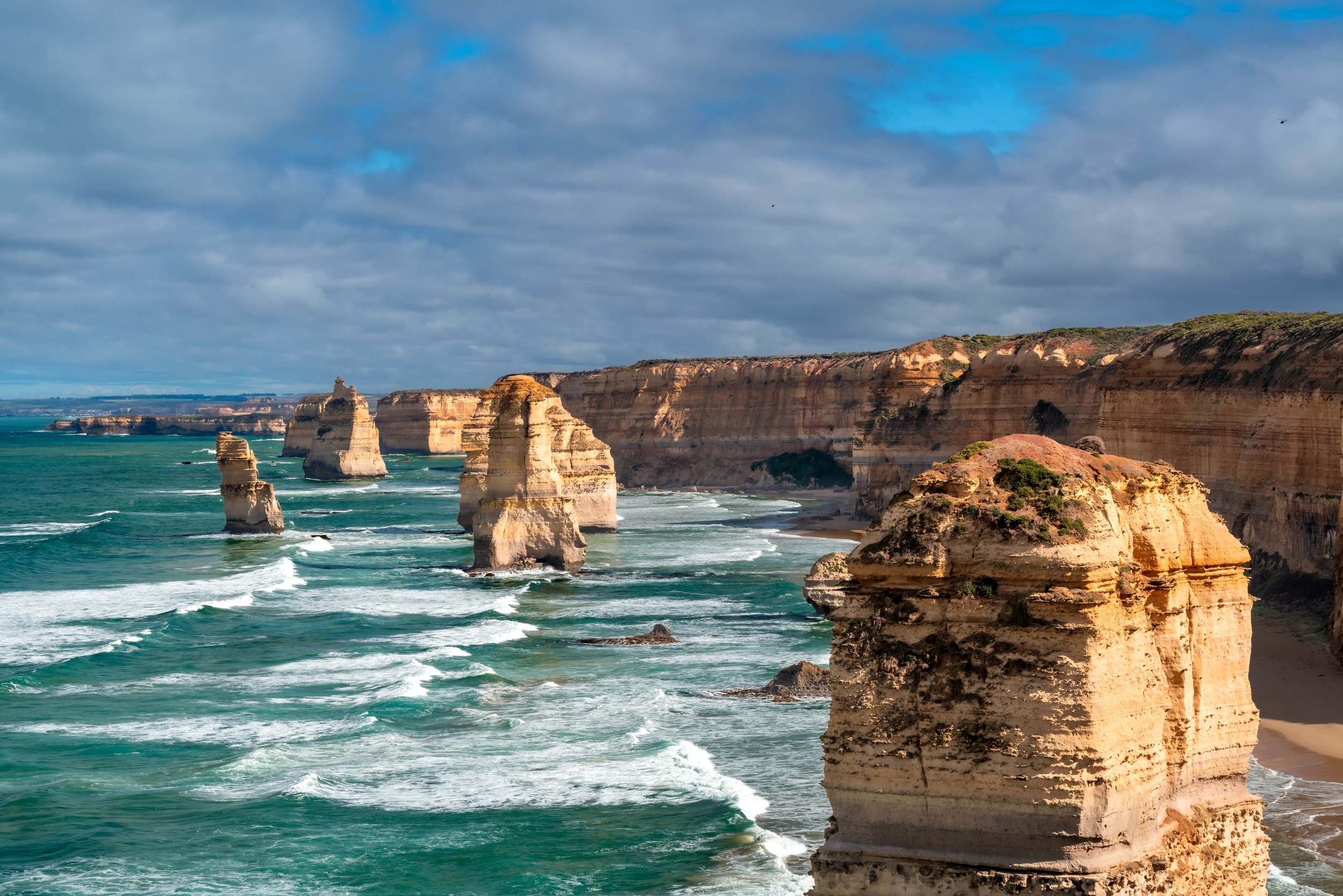 Sandstone monoliths and cliffs stand up out of the ocean. Some are eroding or have eroded.