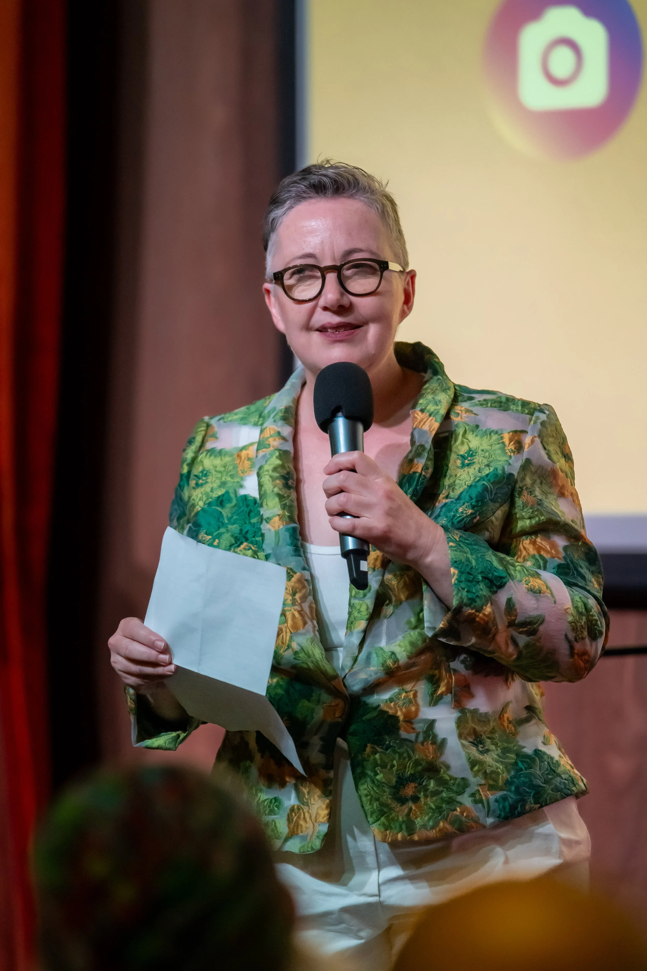 A human in a green jacket speaks into a microphone.