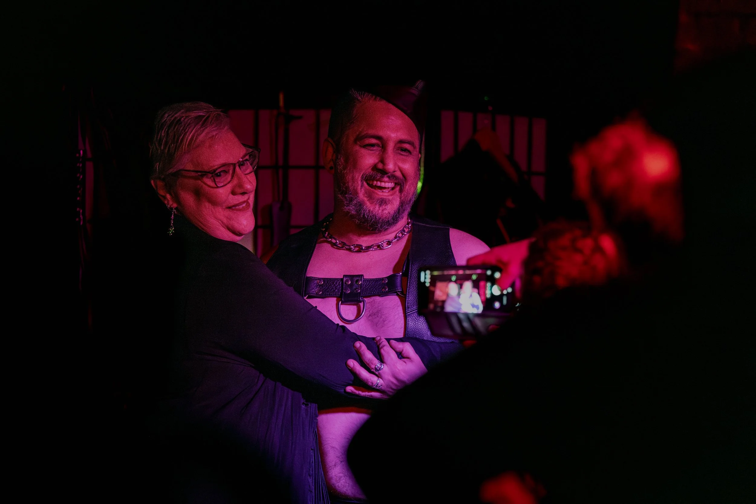 Andrew Rose hugs a human whilst another human takes their photo on their phone.