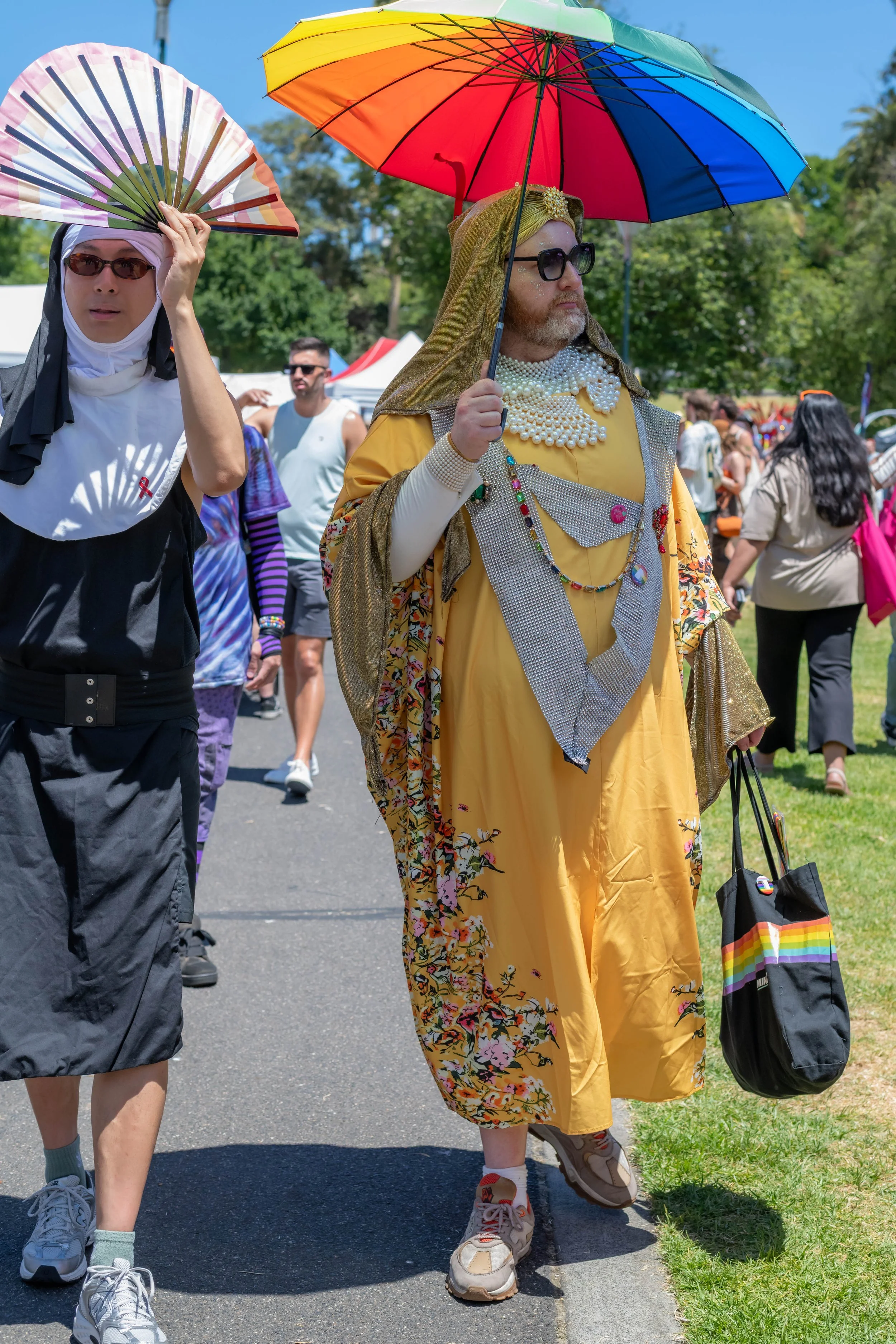 Two humans dressed as nuns. One holds up a fan, the other holds a rainbow umbrella.
