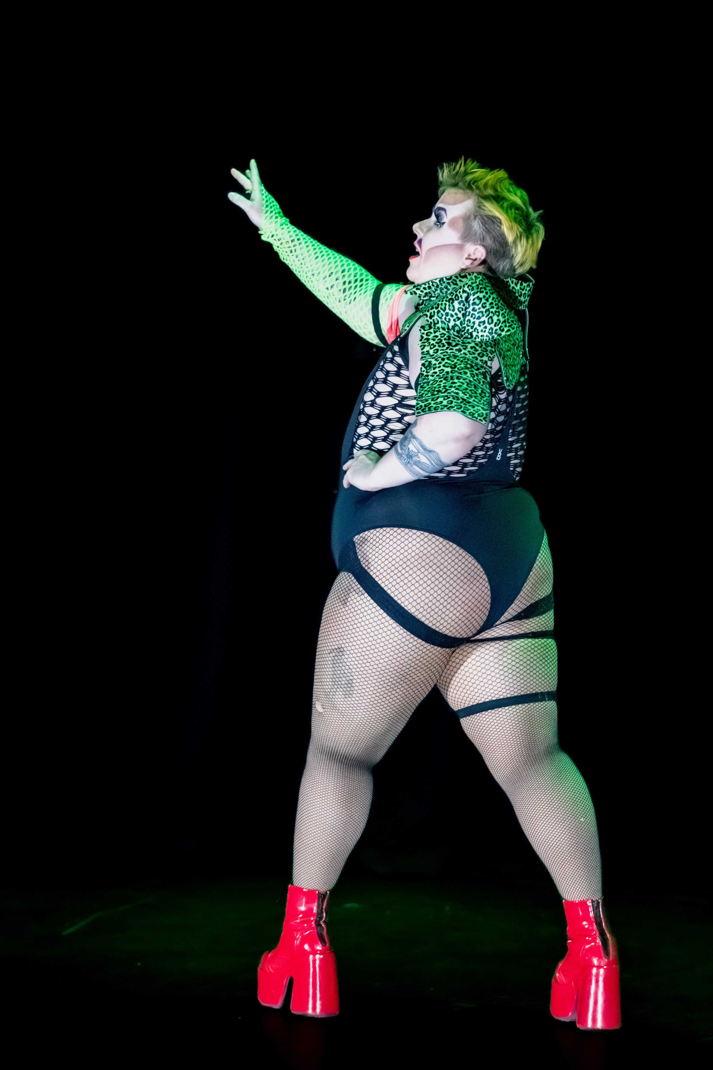 Drag King Jesse Dean turns away from the audience and raises an arm to the sky.