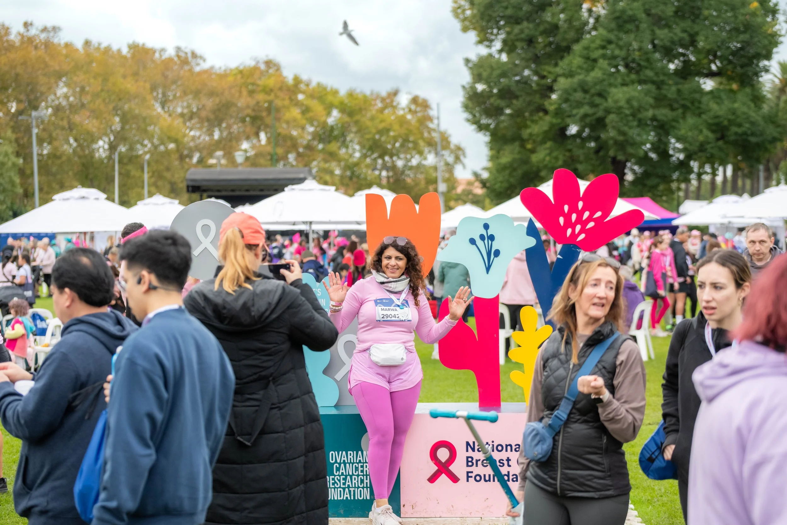 A large crowd of racegoers. One poses in front of the NBCF/OCRF flowers.