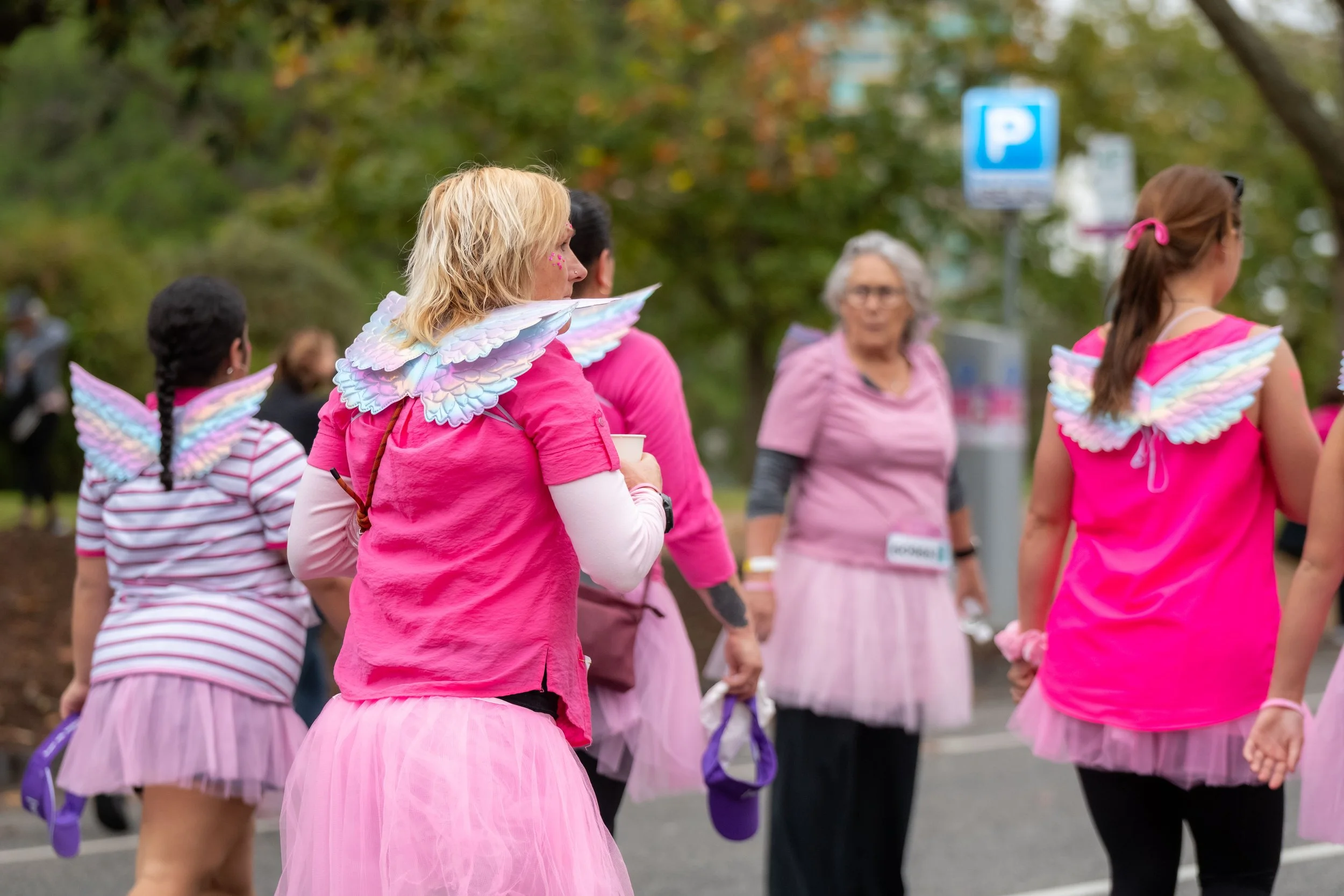 A human wearing pink wears small shimmery wings on their back.