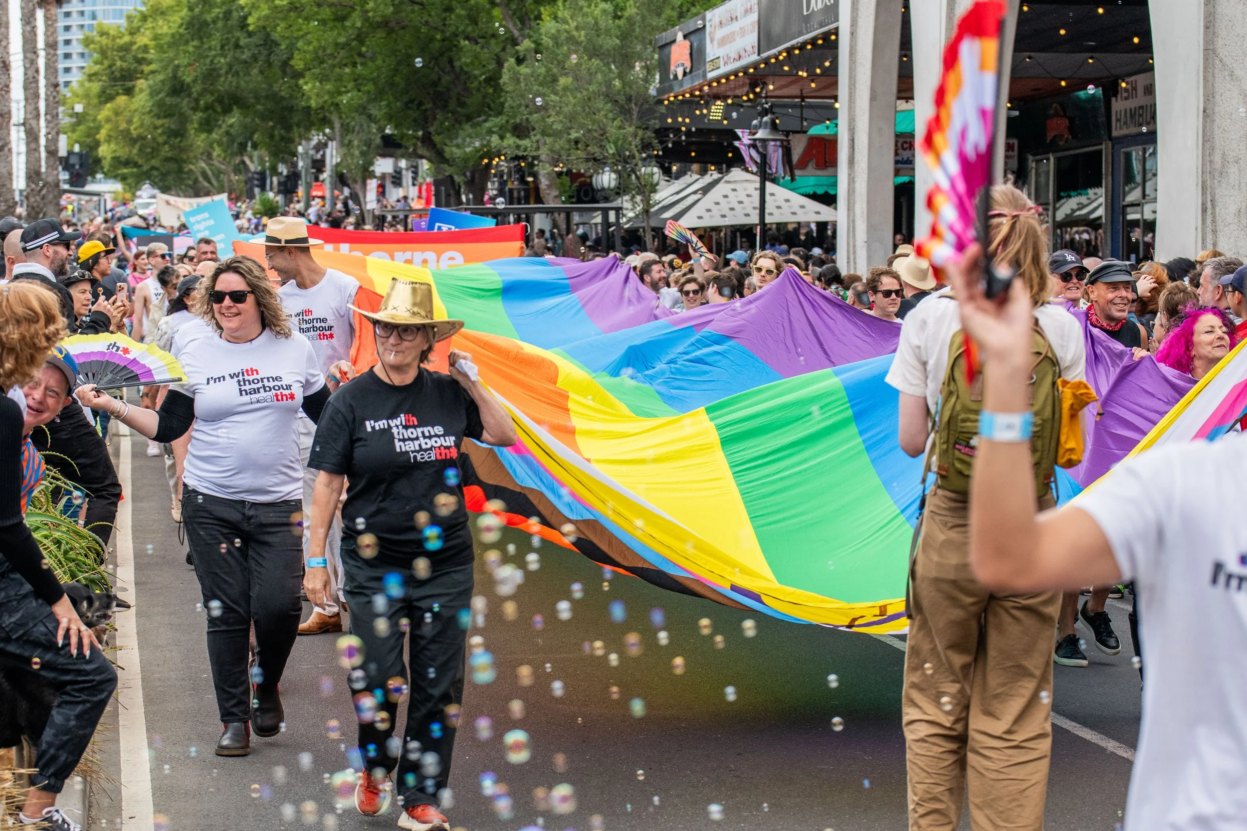 Bubbles flow over a large progress pride flag being carried by multiple marchers.