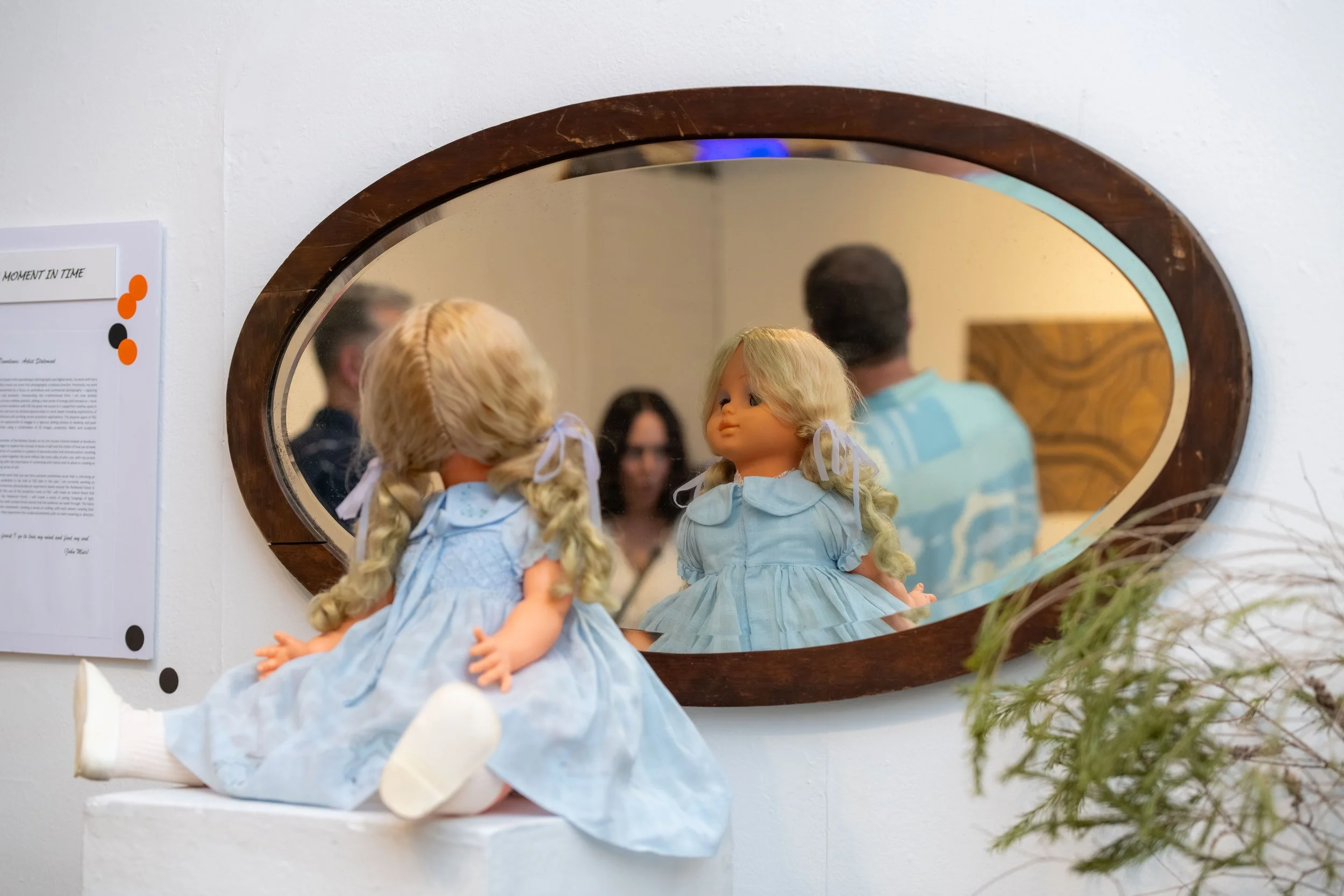 A doll with its head backwards looks into a mirror.
