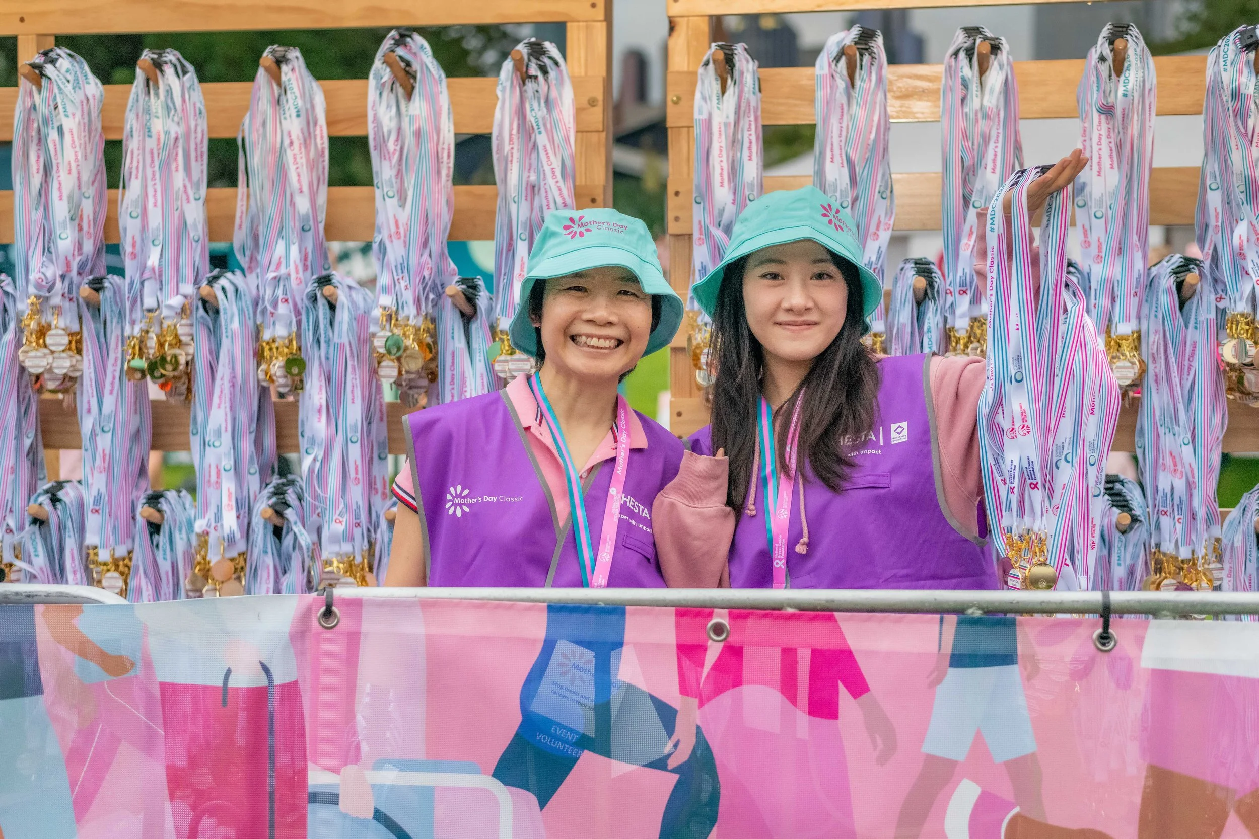 Two volunteers hold armfuls of medals.