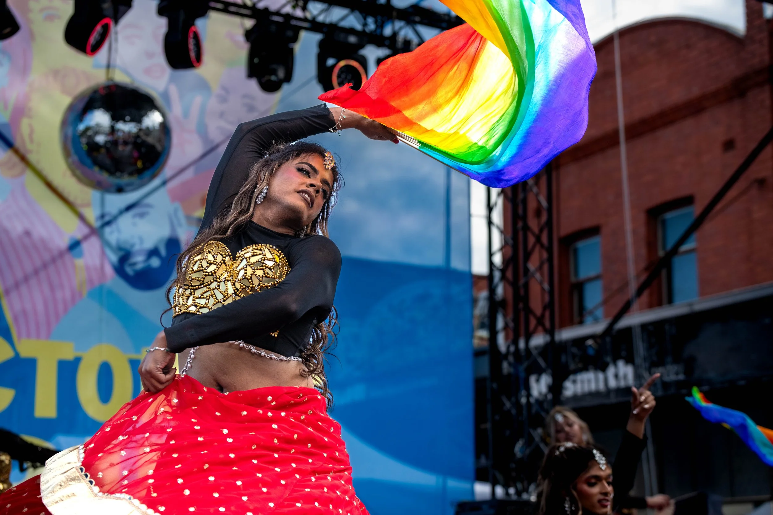 A dancer from Karma Dance bends backward as they toss a rainbow flag in the air.