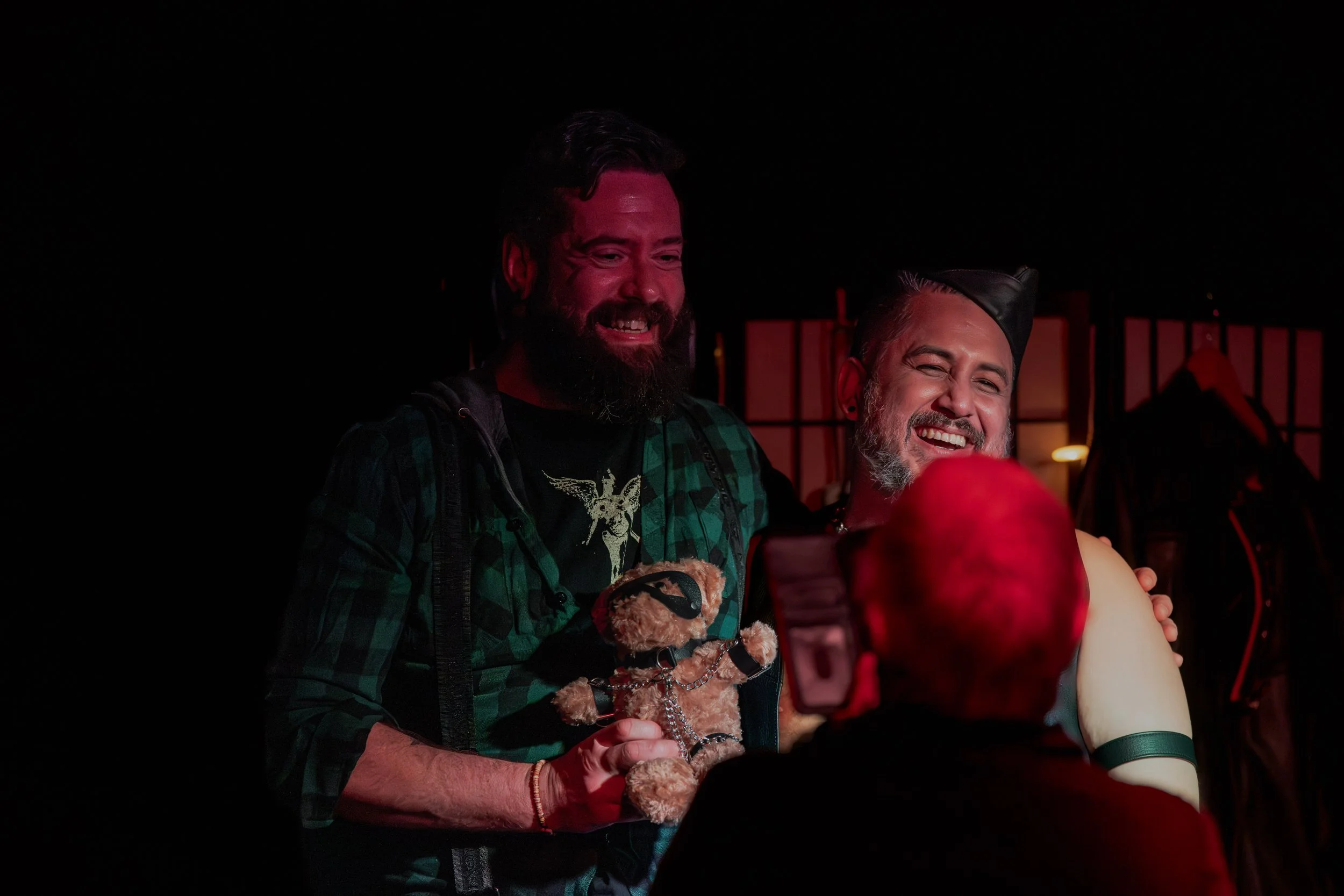 Andrew Rose hugs a taller human who holds onto a kinky teddy bear.