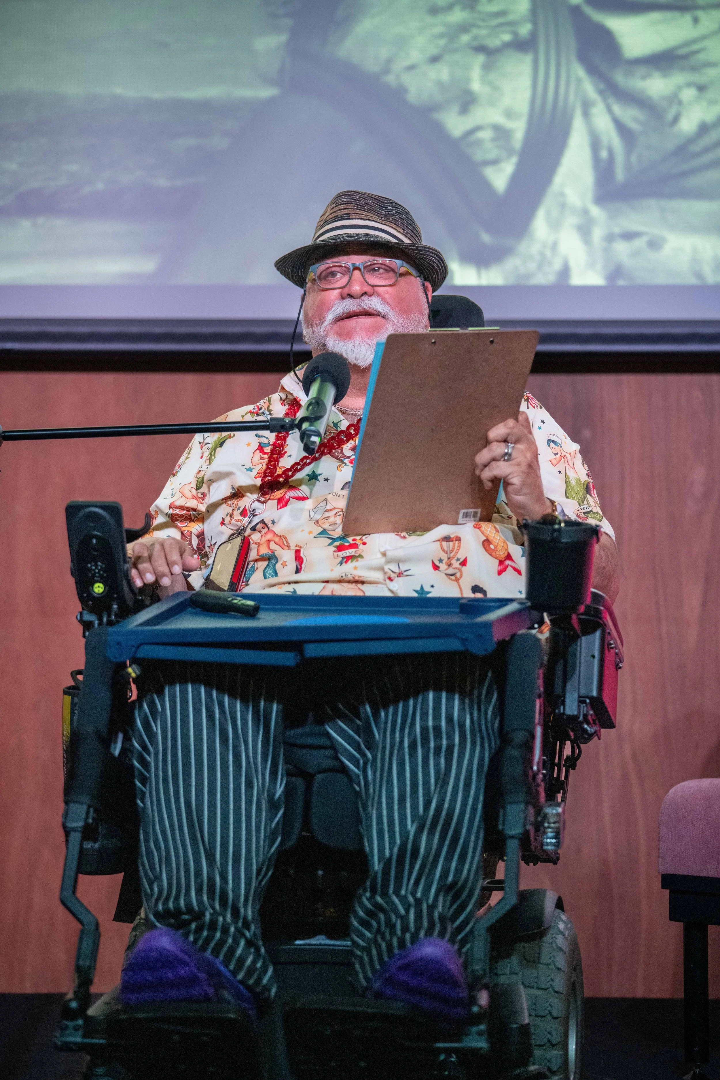A human in a wheelchair gives a speech from notes.