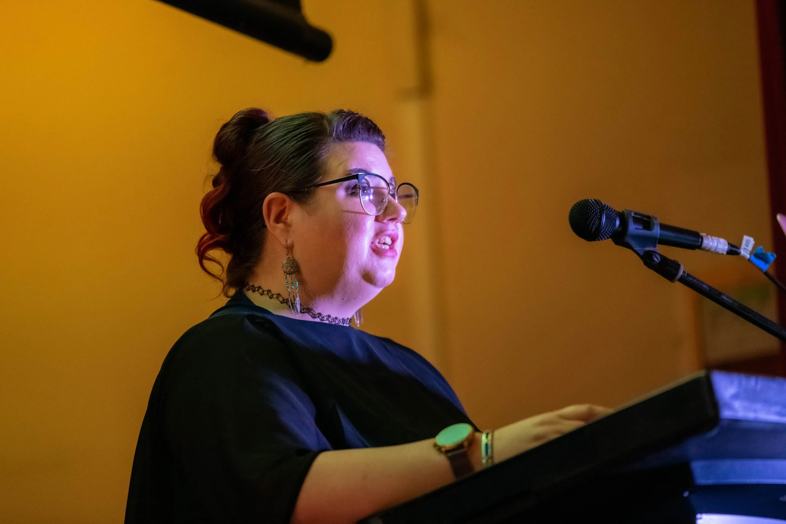 Meghan Aponte stands behind a lecturn and speaks into a microphone.