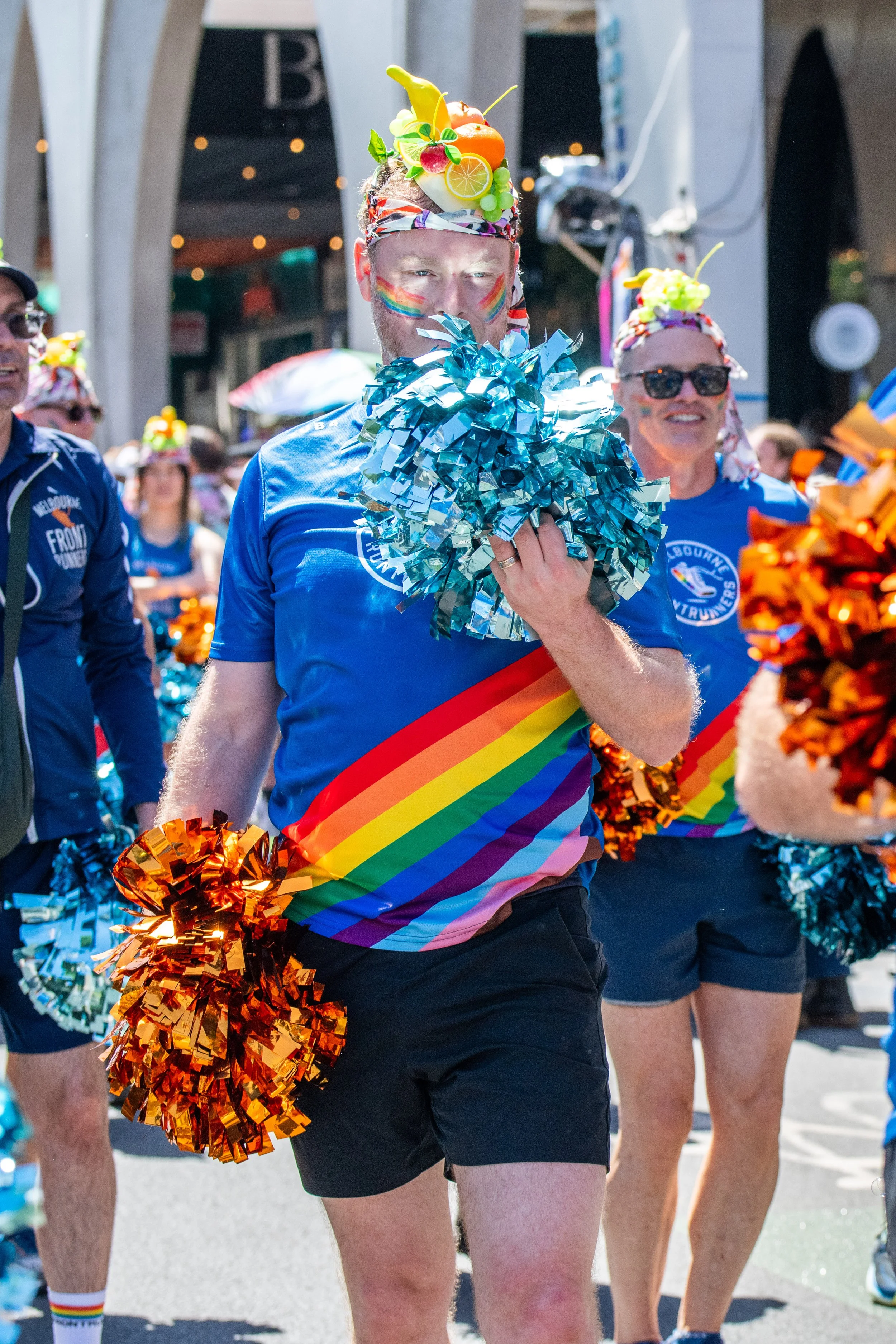 A human holds a blue and an orange pom pom. The blue pom reflects in their face.