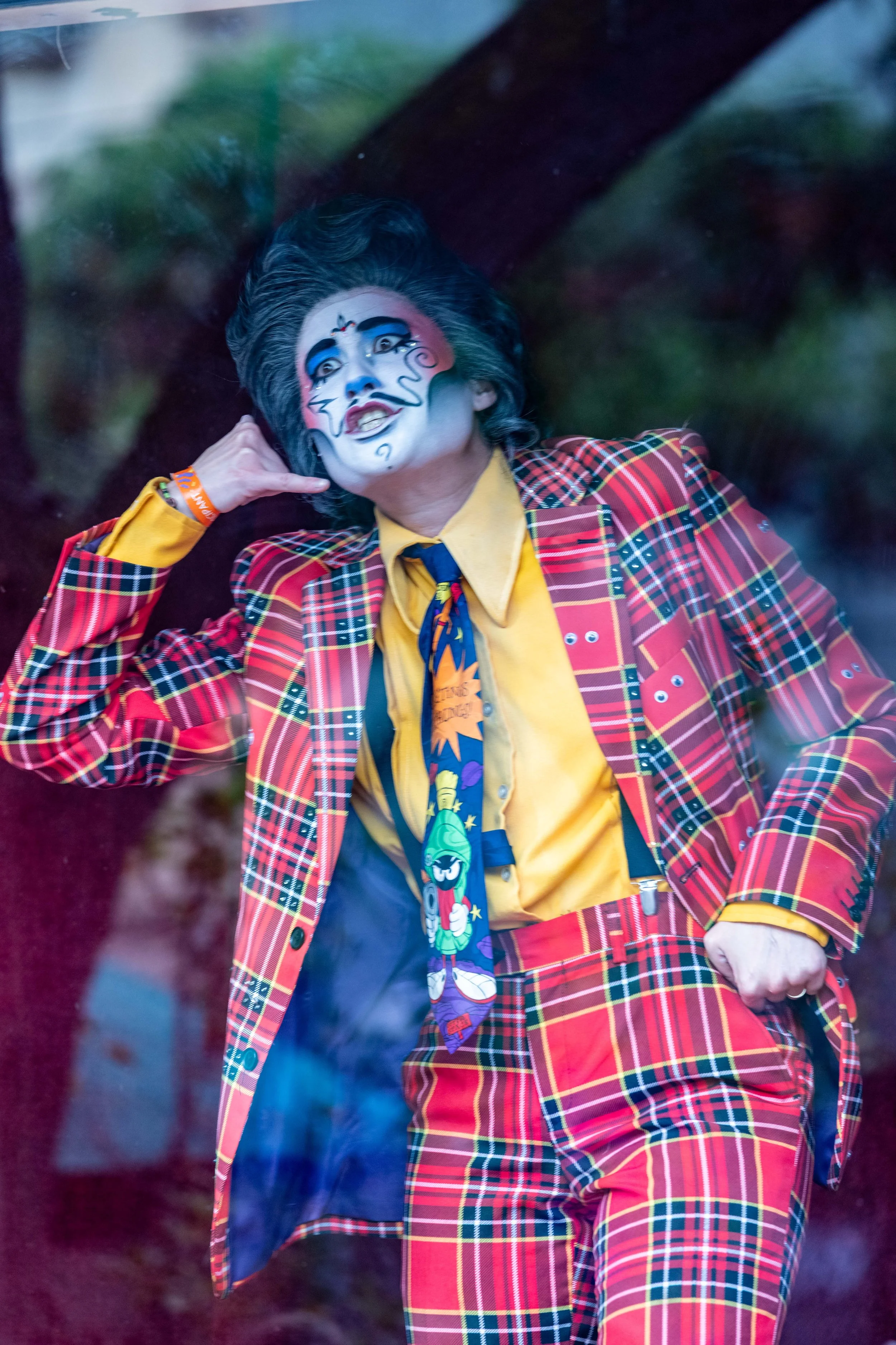 Drag king Randy Roy wears a red plaid suit and poses behind a glass window.