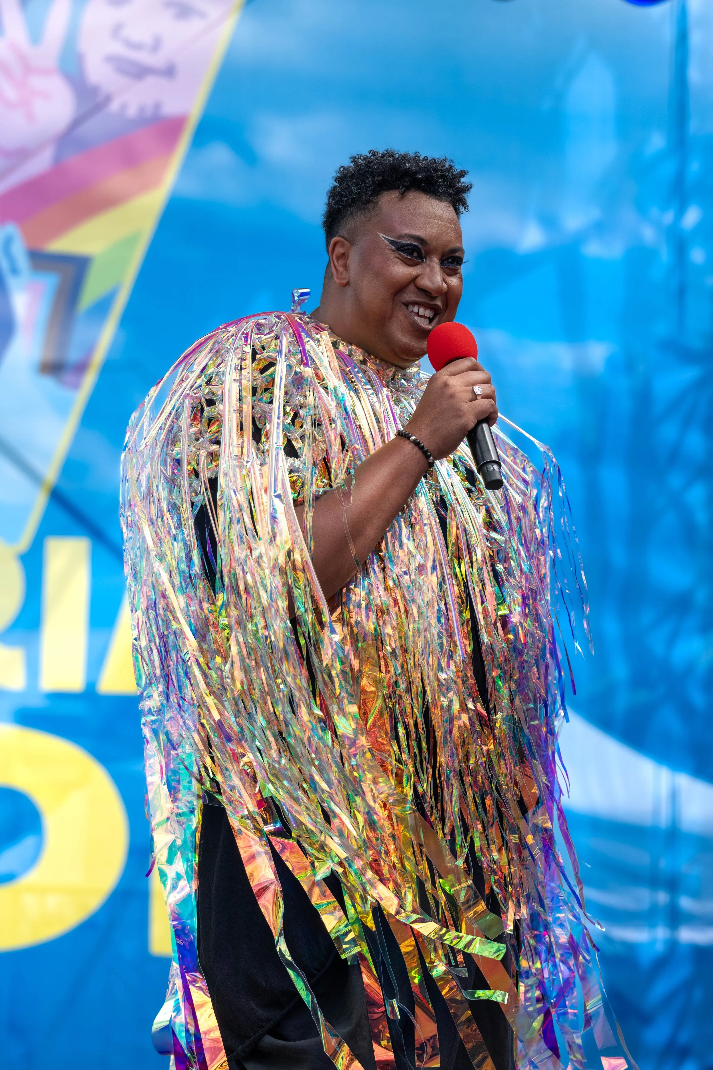 Samuel Gaskin wears a swishy chromatic outfit and talks into a microphone.