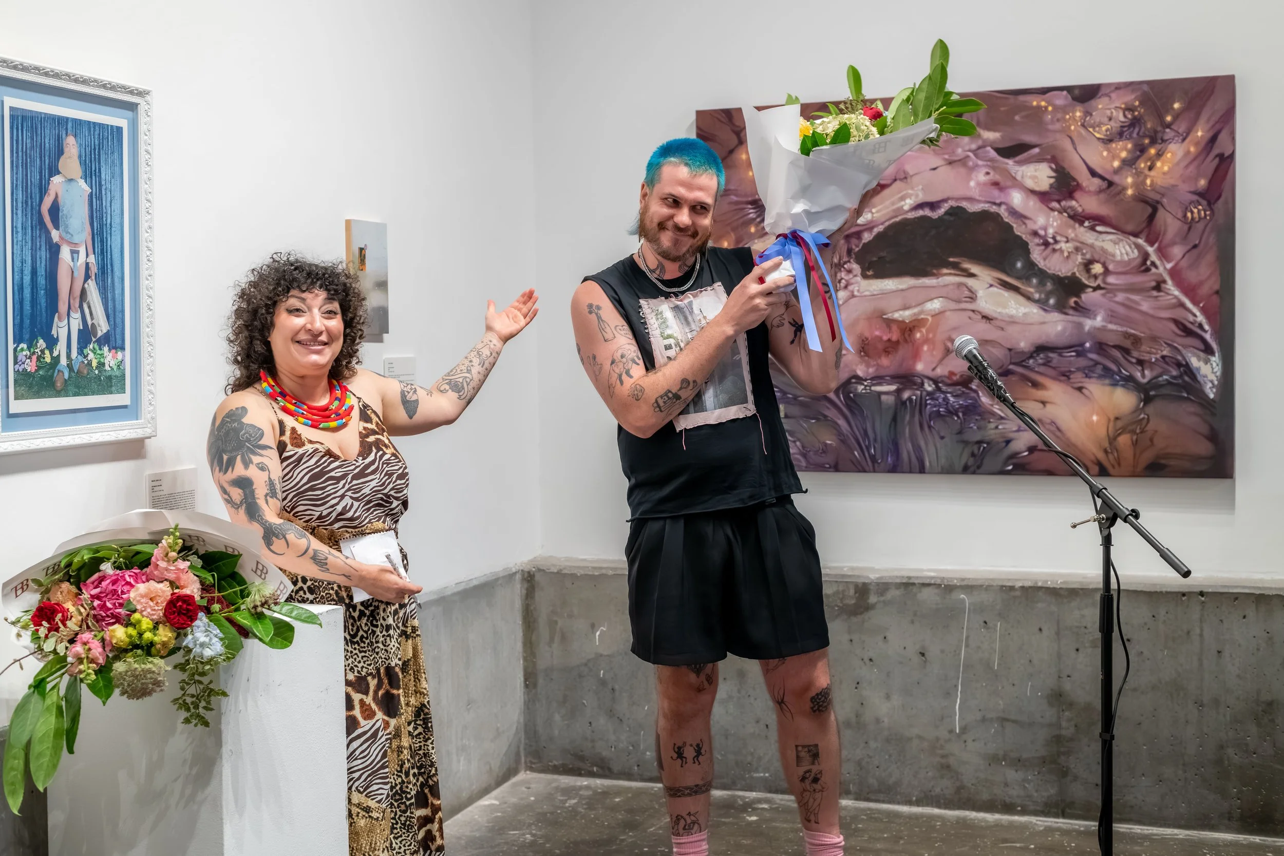 A human announces another human who has won the main prize. J Davies holds a bouquet of flowers.