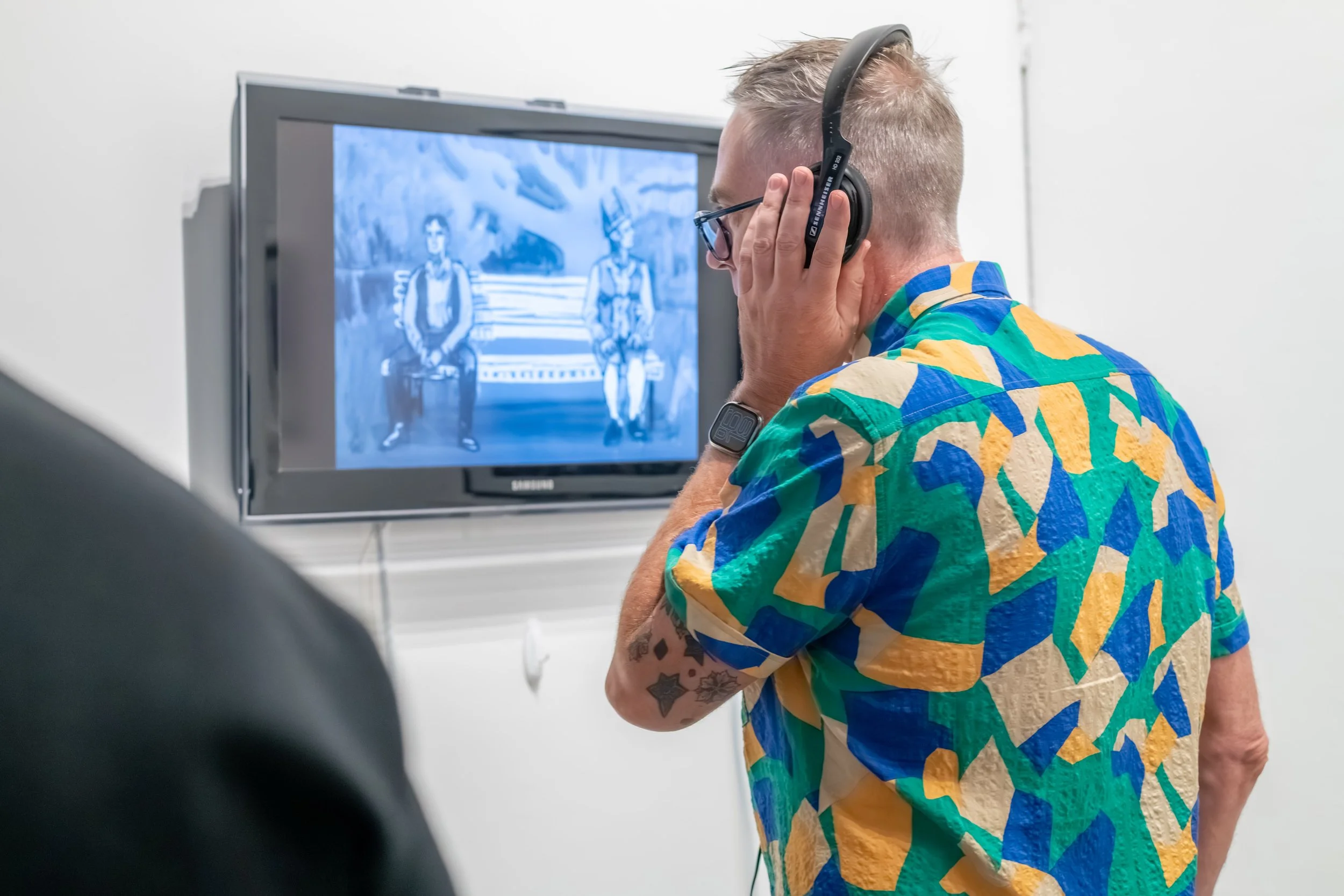 A human looks at a tv screen. They are listening to the artwork through headphones.