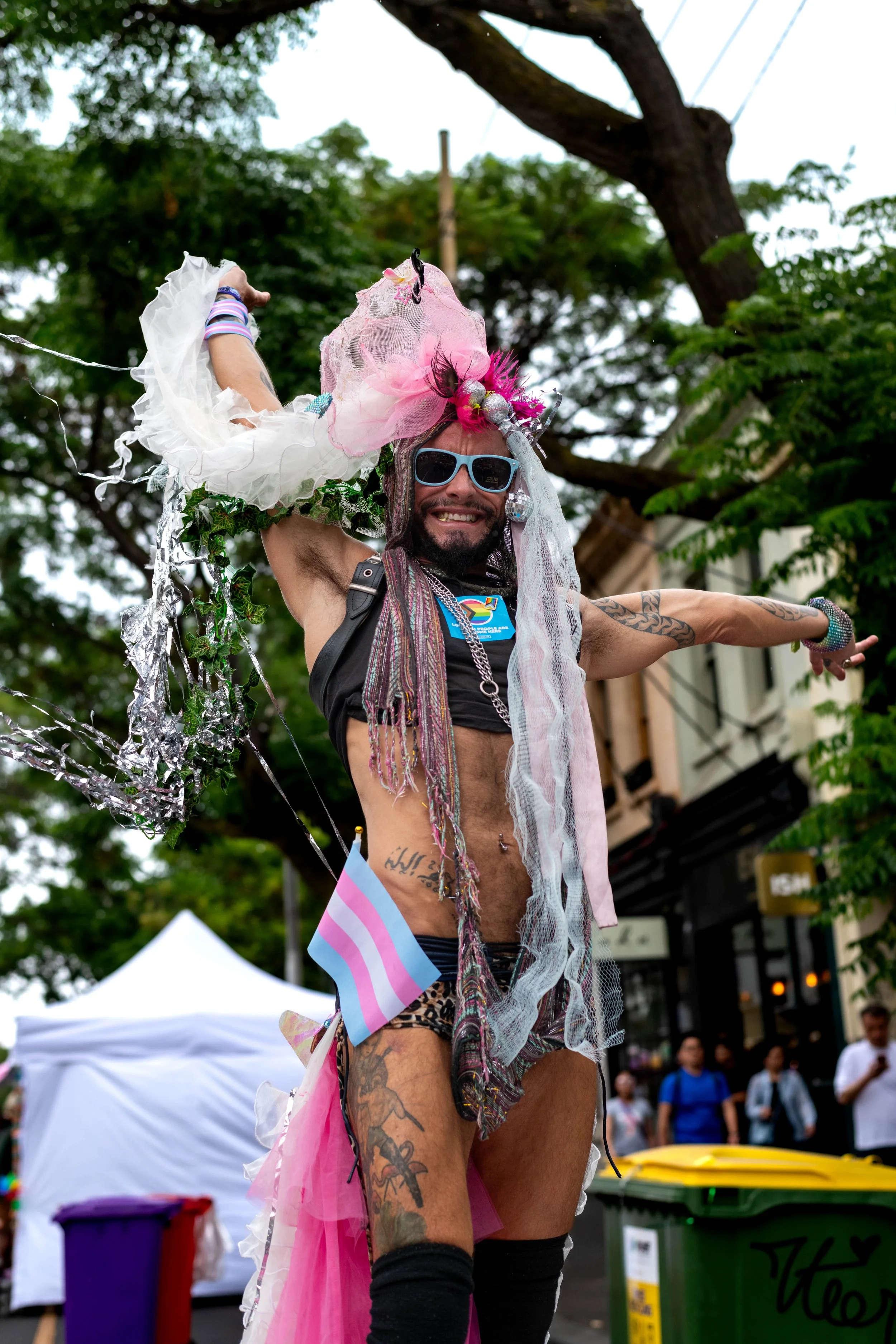 Danny standing tall up on a table with outstretched arms. They have a trans flag in their shorts.