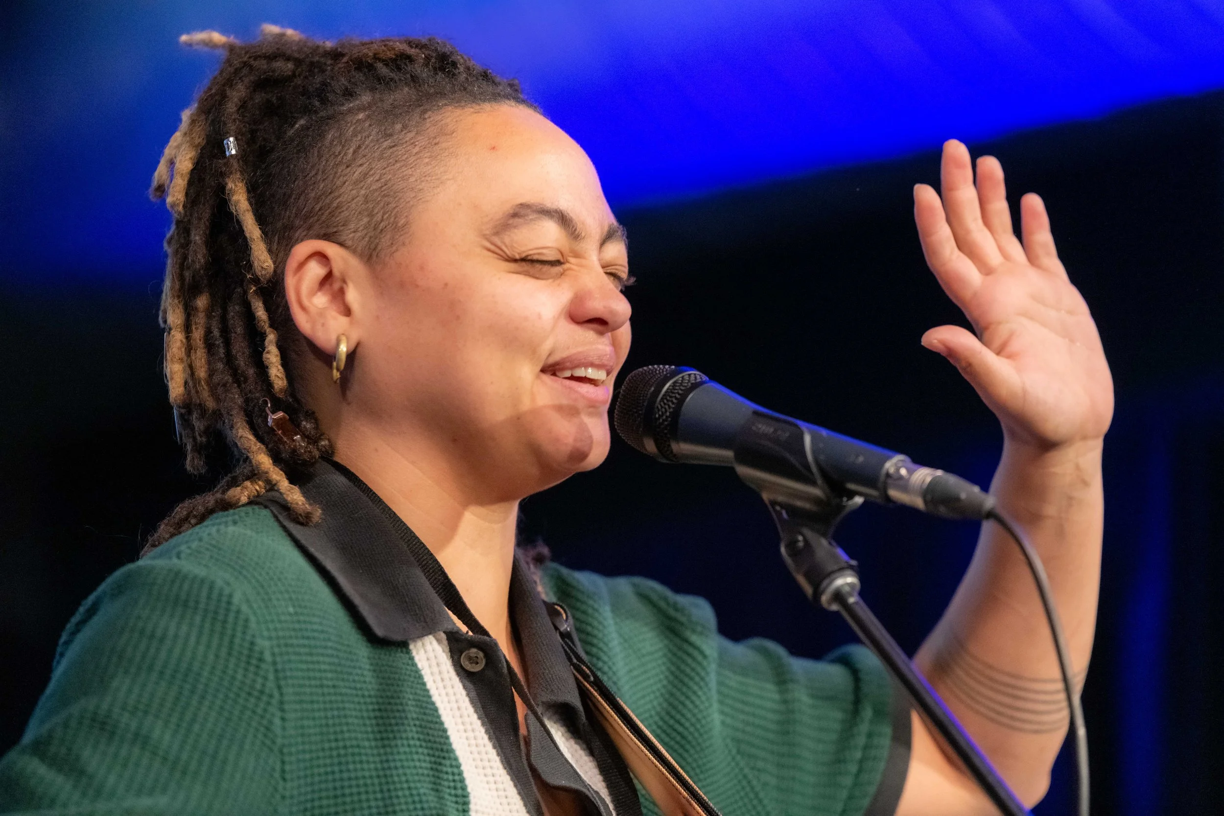 Close up of a human singing into a microphone, their hand is raised and their eyes are closed.