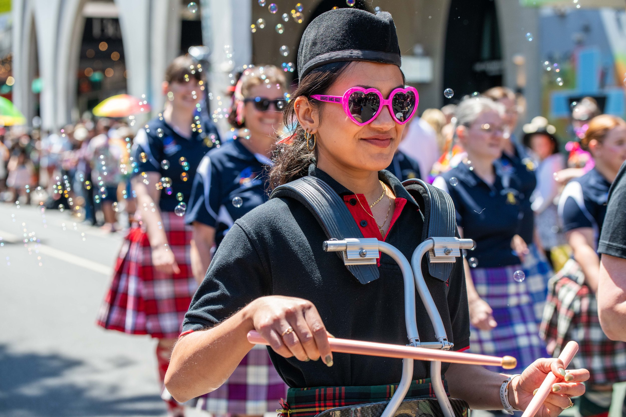A band member wearing pink love heart sunglasses marches through bubbles.