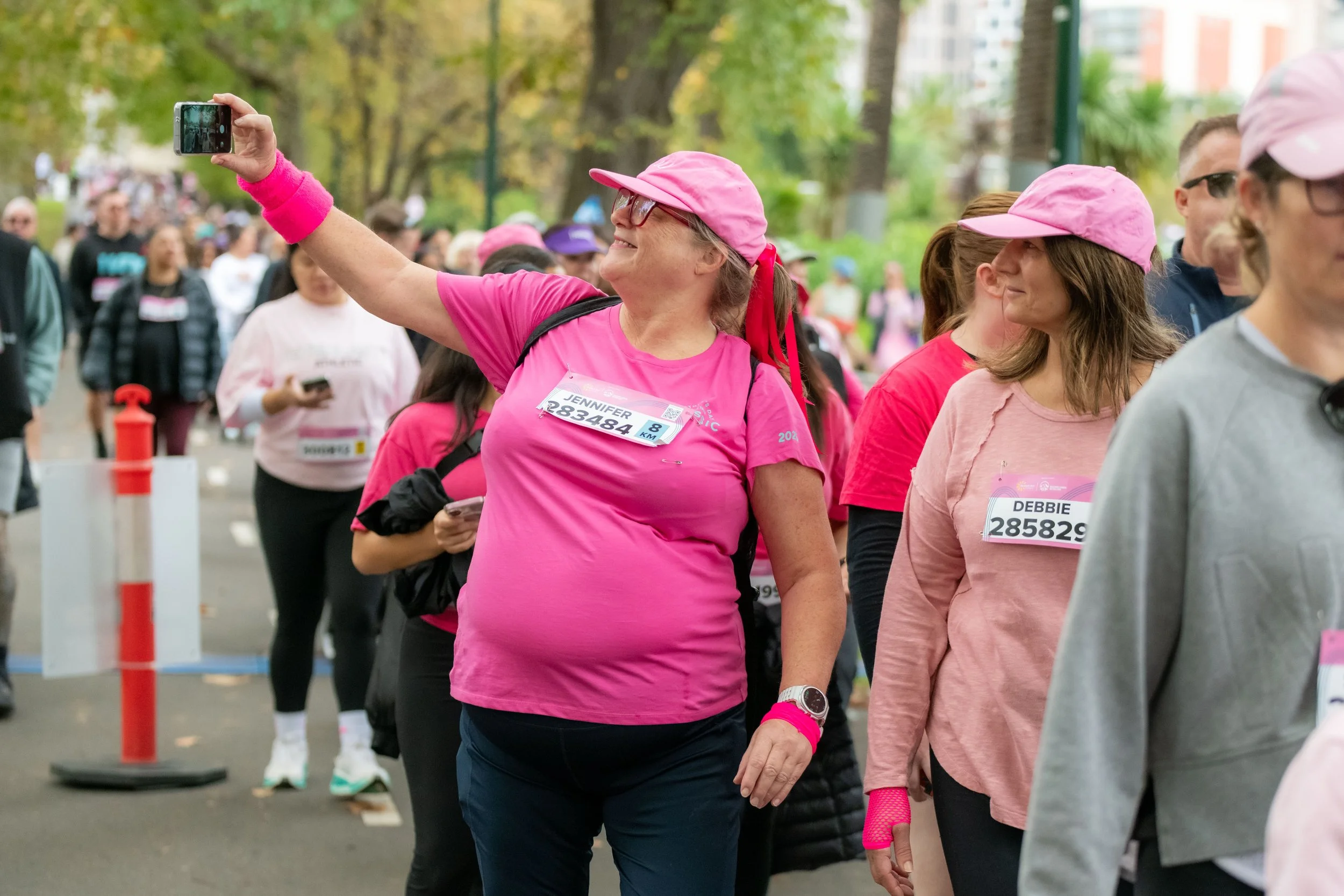 A racegoer wearing pink takes a selfie with their phone.