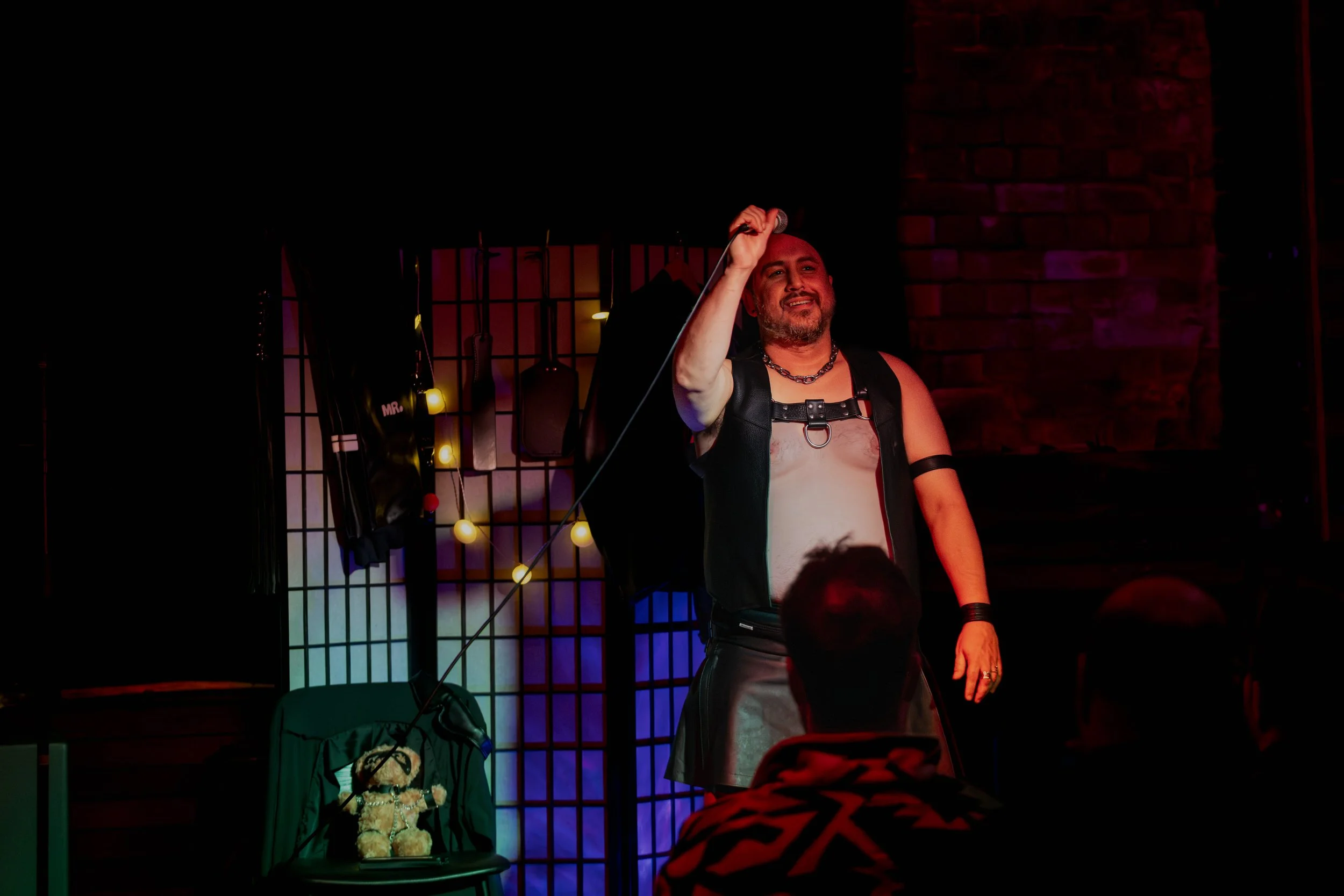 Andrew Rose holding up a microphone. A teddy bear in leathers sits on a chair.