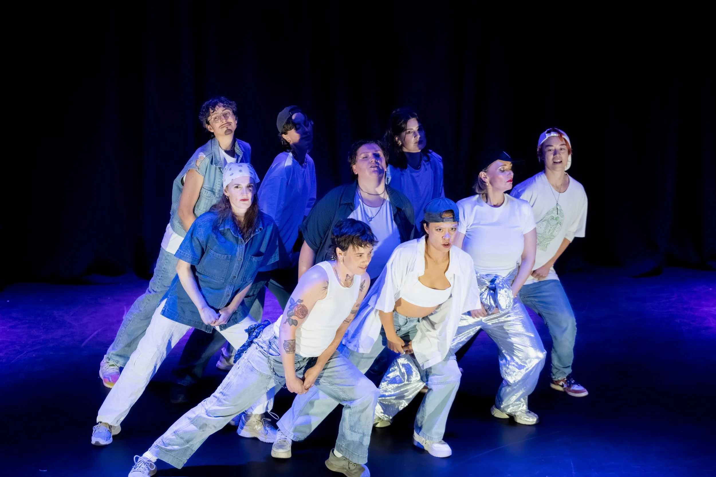 A group of dancers in denim form a triangle and lean to the right in unison.