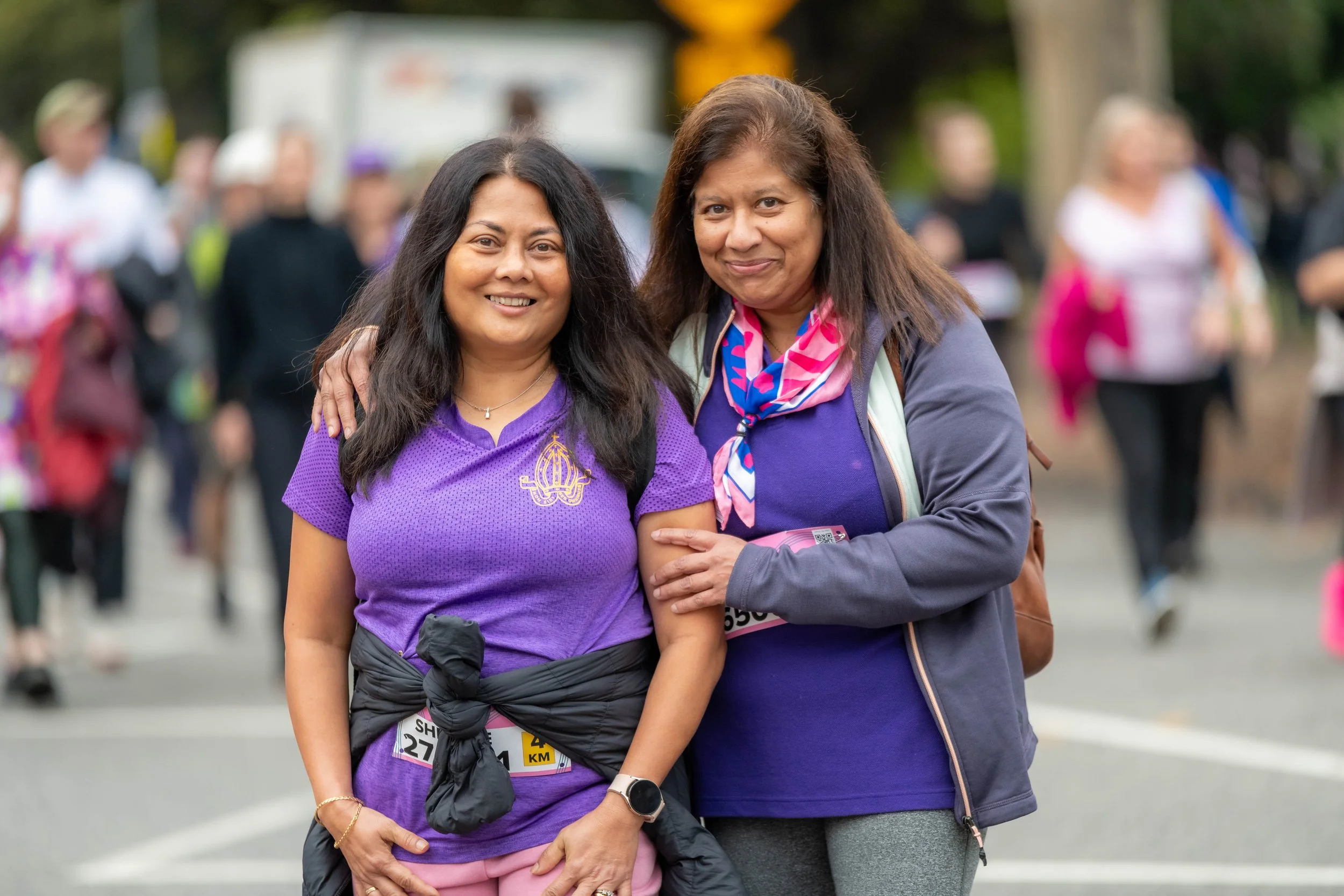 Two racegoers wearing purple smile at the camera.