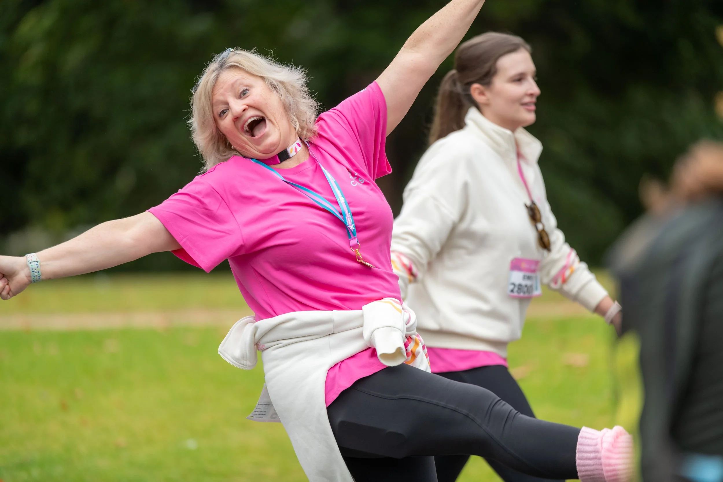 A racegoer wearing a pink tee kicks up their leg and laughs at the camera.